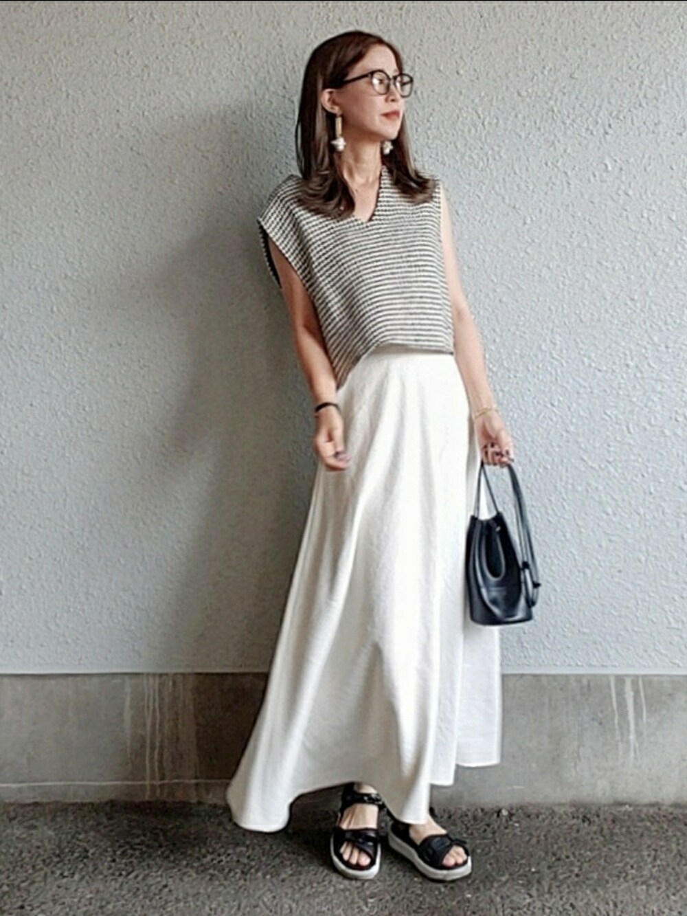 ブラック系のベスト、ホワイト系のスカート、ブラック系のハンドバッグを着用したレディースの夏コーディネートの2枚目の写真