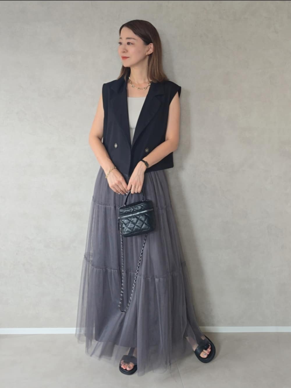 ブラック系のベスト、グレー系のスカート、ブラック系のサンダルを着用したレディースの秋コーディネートの2枚目の写真