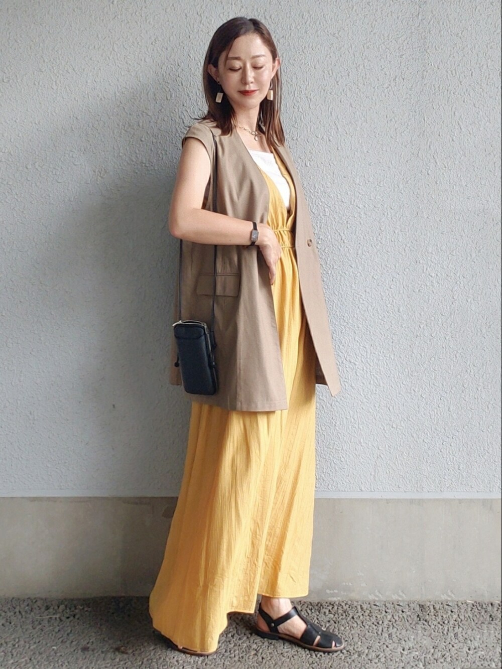 イエロー系のワンピース、ブラウン系のベスト、ブラック系のサンダルを着用したレディースの夏コーディネートの2枚目の写真