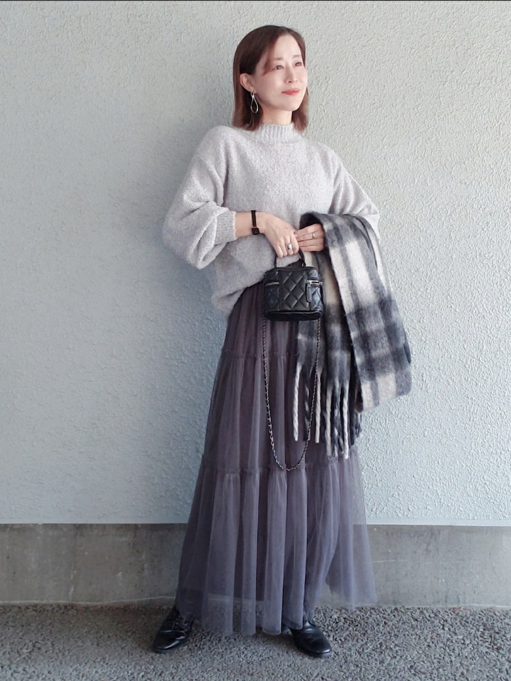 グレー系のニット/セーター、グレー系のスカート、ブラック系のバッグを着用したレディースの冬コーディネートの3枚目の写真