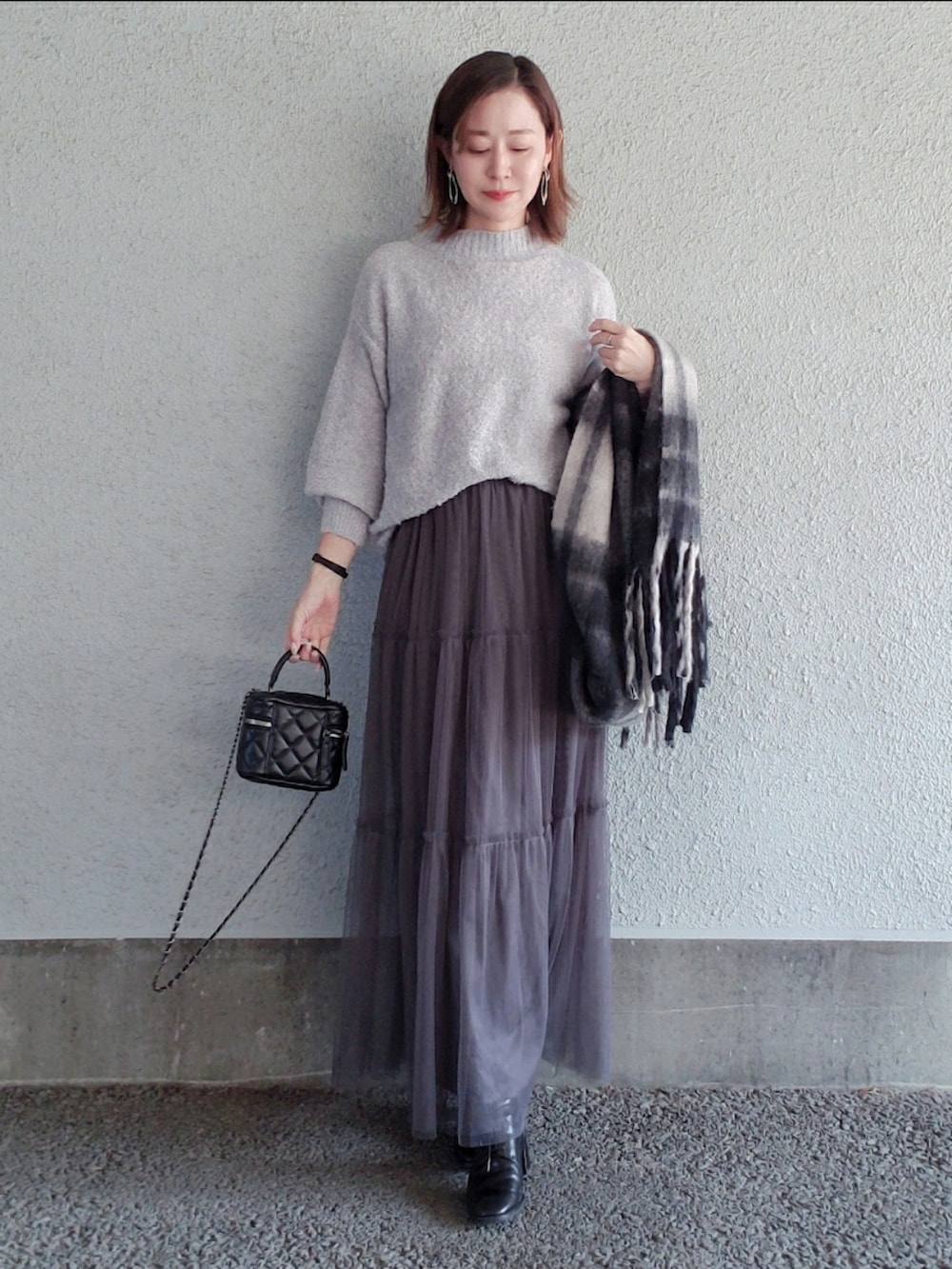 グレー系のニット/セーター、グレー系のスカート、ブラック系のバッグを着用したレディースの冬コーディネートの2枚目の写真