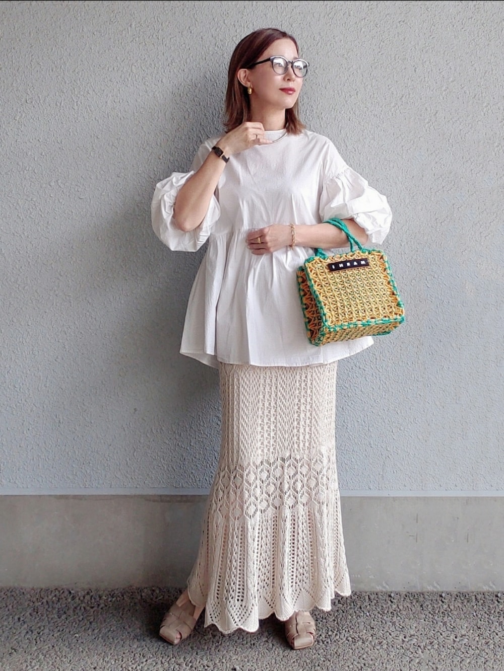 イエロー系のバッグ、ホワイト系のスカート、グレー系のサンダルを着用したレディースの春コーディネートの2枚目の写真