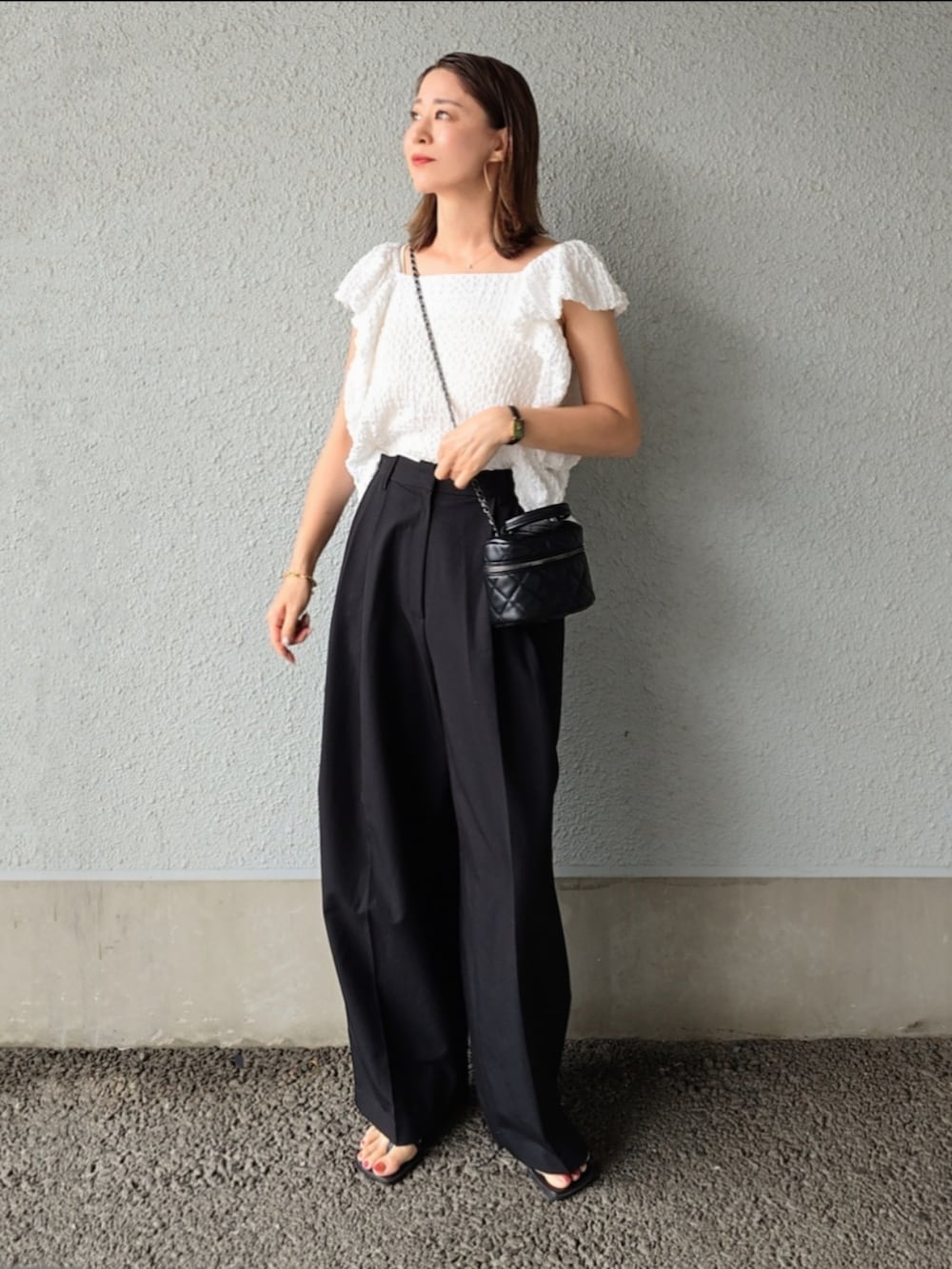 ホワイト系のシャツ/ブラウス、ブラック系のスラックス、ブラック系のサンダルを着用したレディースの夏コーディネートの2枚目の写真