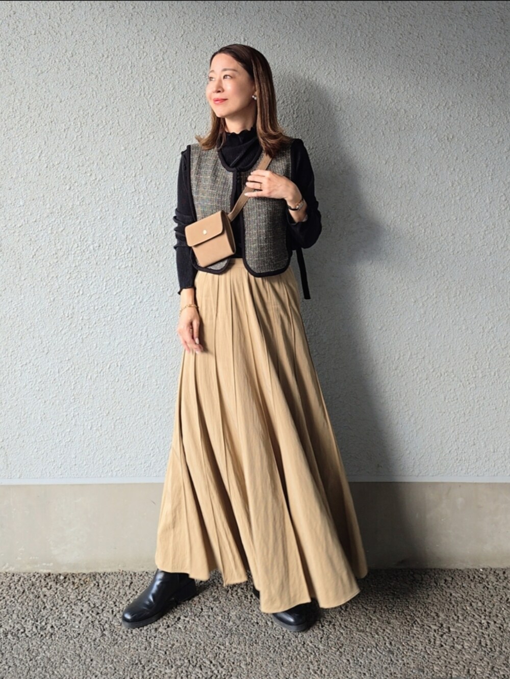 ベージュ系のスカート、ベージュ系のショルダーバッグ、ブラック系のベストを着用したレディースの秋コーディネートの4枚目の写真