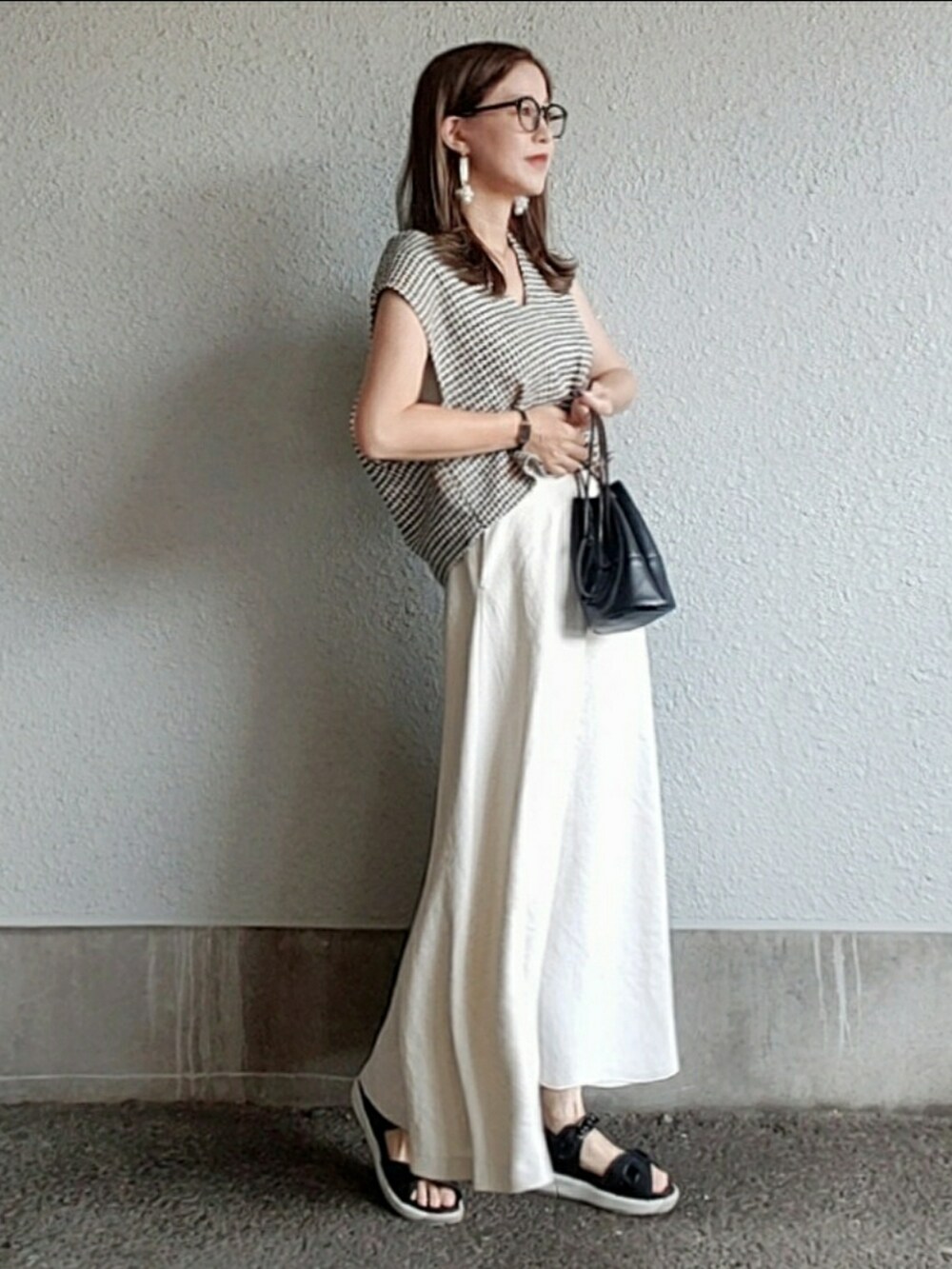 ブラック系のベスト、ホワイト系のスカート、ブラック系のハンドバッグを着用したレディースの夏コーディネートの3枚目の写真