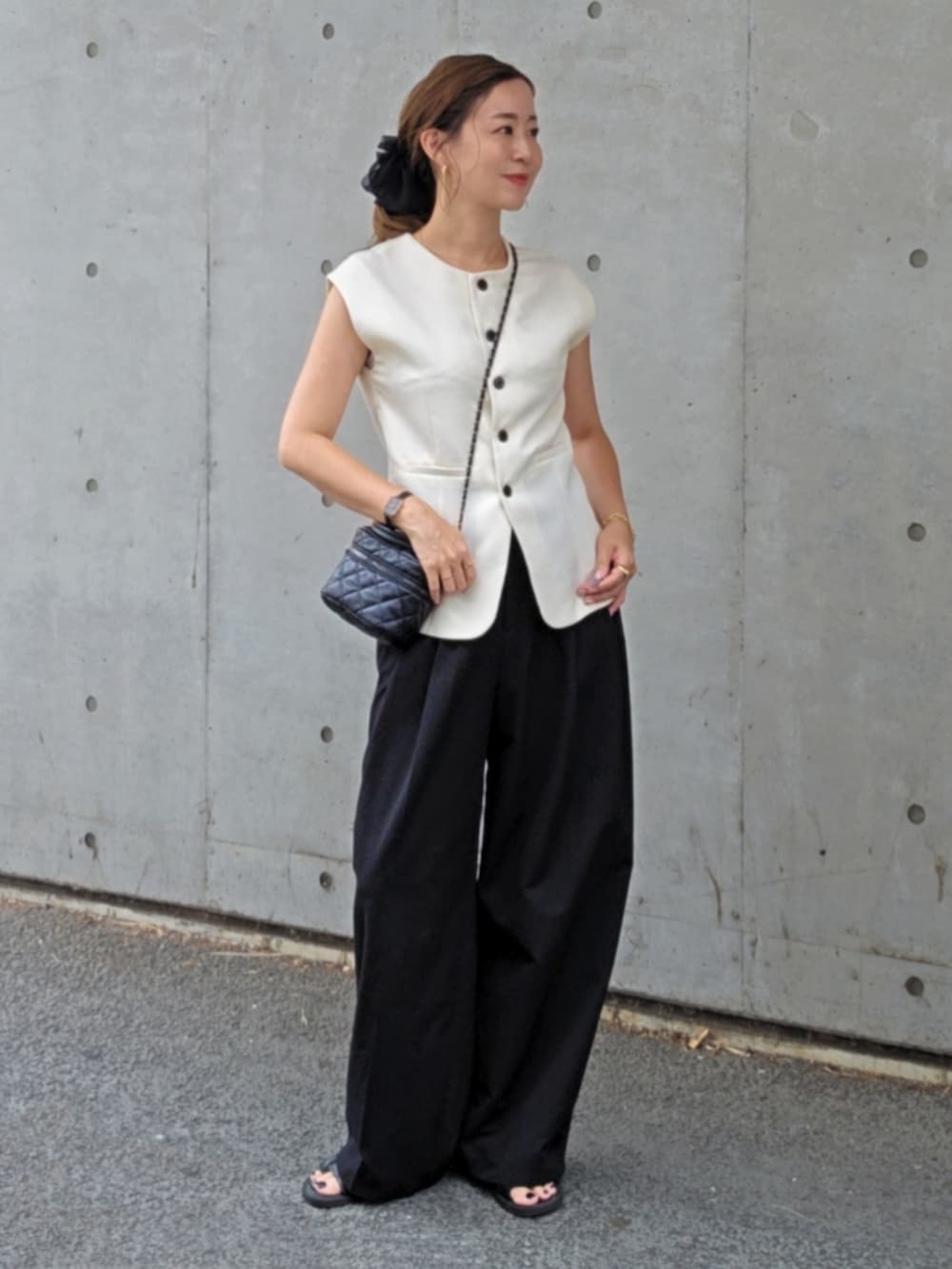 ホワイト系のベスト、ブラック系のスラックス、ブラック系のサンダルを着用したレディースの夏コーディネートの2枚目の写真