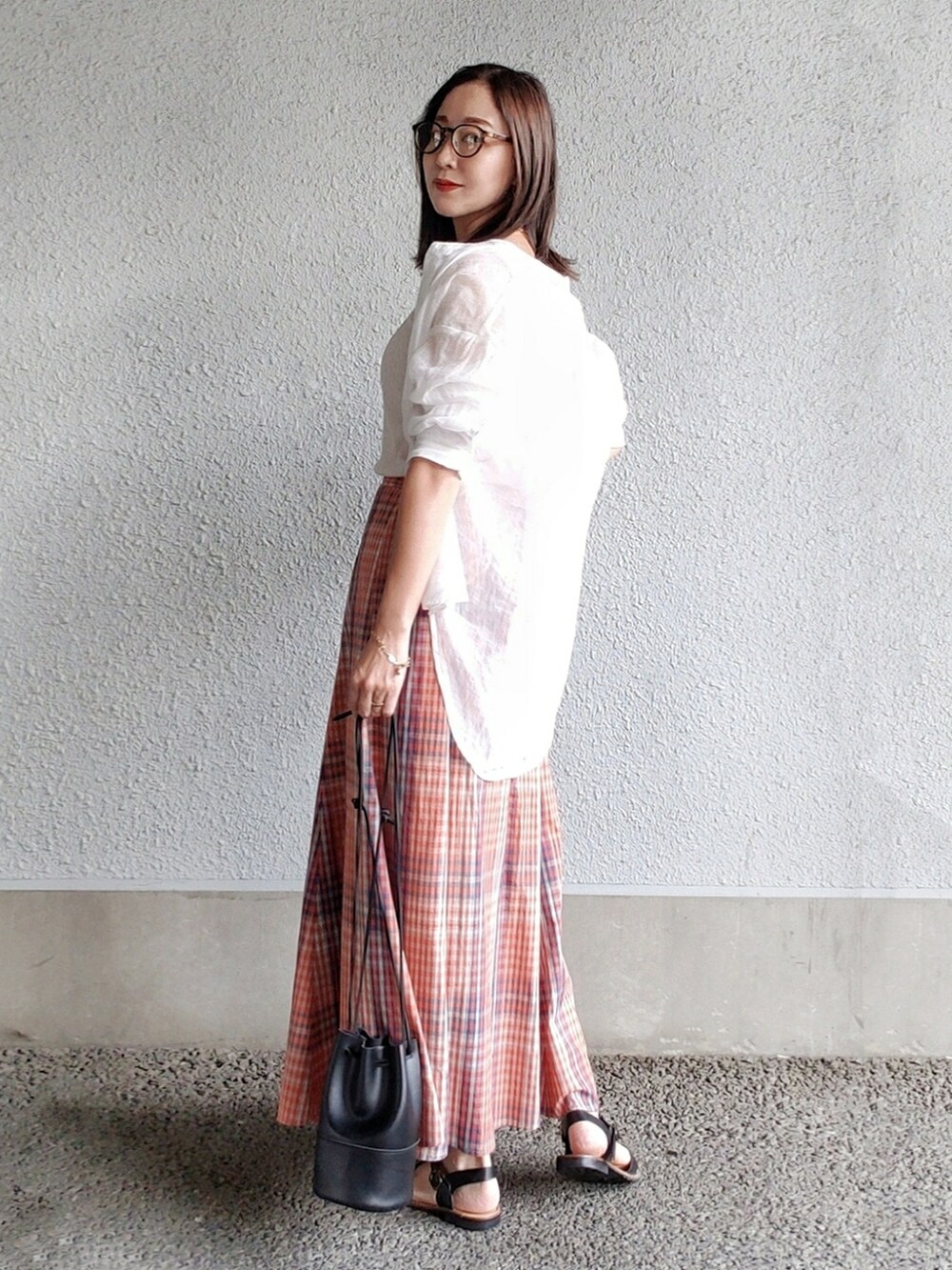 オレンジ系のスカート、ブラック系のハンドバッグ、ブラック系のサンダルを着用したレディースの夏コーディネートの2枚目の写真