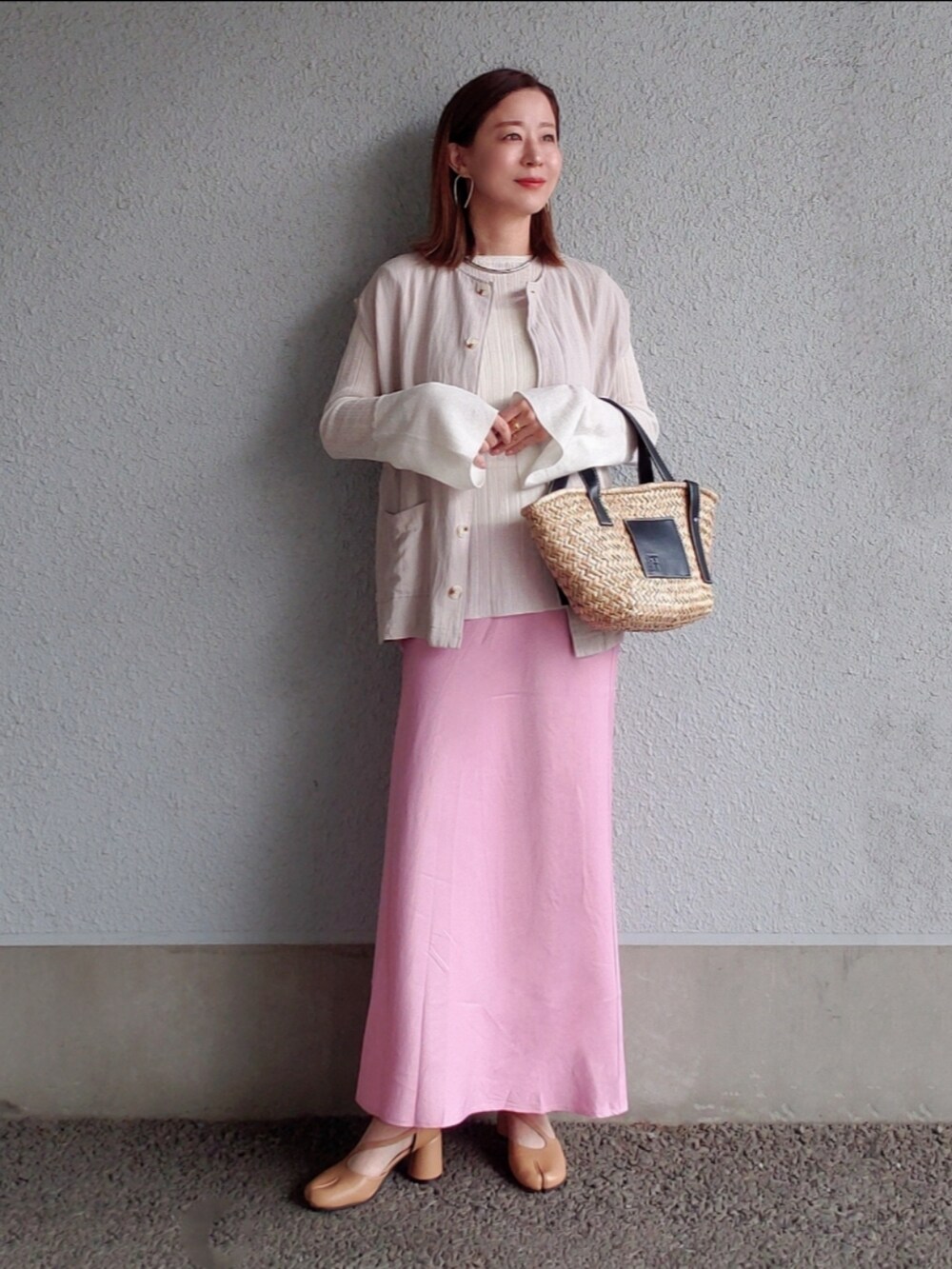 ピンク系のスカート、ブラック系のかごバッグ、ホワイト系のニット/セーターを着用したレディースの春コーディネートの2枚目の写真
