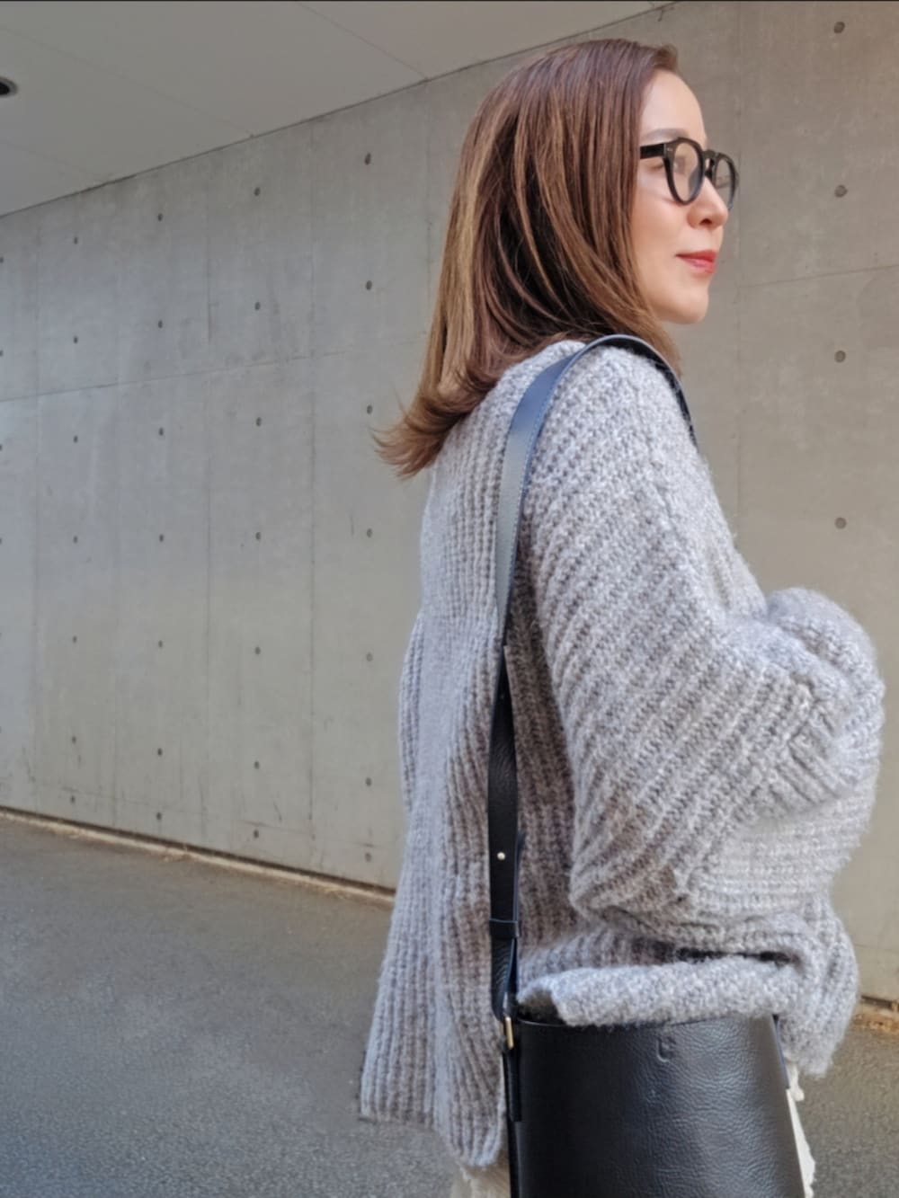 グレー系のニット/セーター、ホワイト系のスカート、ブラック系のバッグを着用したレディースの冬コーディネートの2枚目の写真