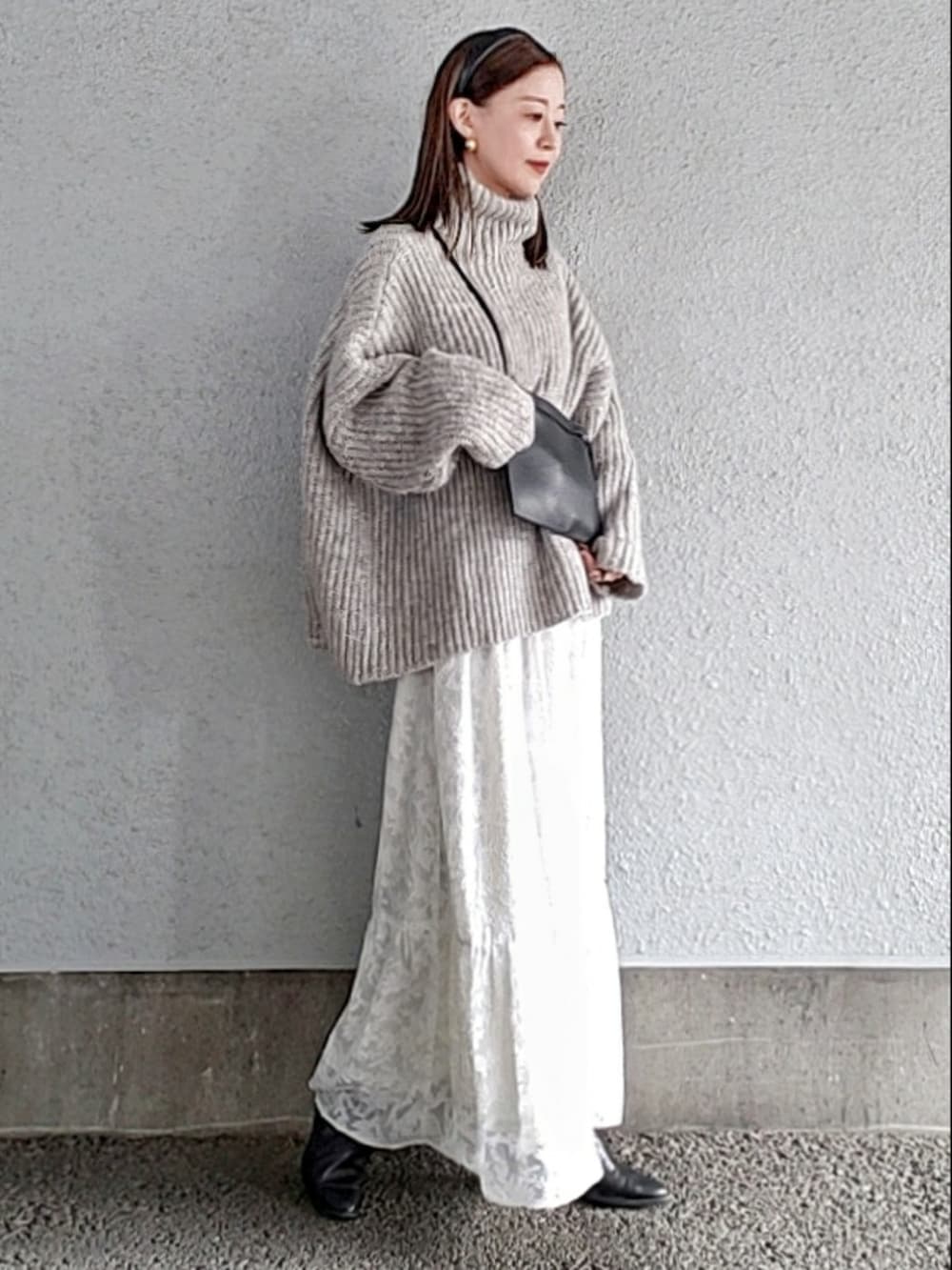 グレー系のニット/セーター、ホワイト系のスカート、ブラック系のブーツを着用したレディースの冬コーディネートの2枚目の写真