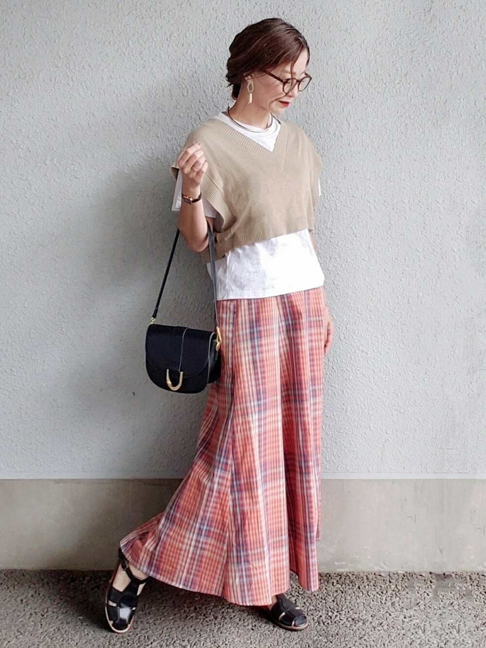 ベージュ系のベスト、オレンジ系のスカート、ブラック系のサンダルを着用したレディースの春コーディネートの2枚目の写真