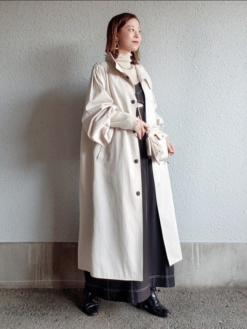 ホワイト系のトレンチコート、ブラック系のワンピース/ドレス、ブラック系のブーツを着用したレディースの春コーディネートの2枚目の写真