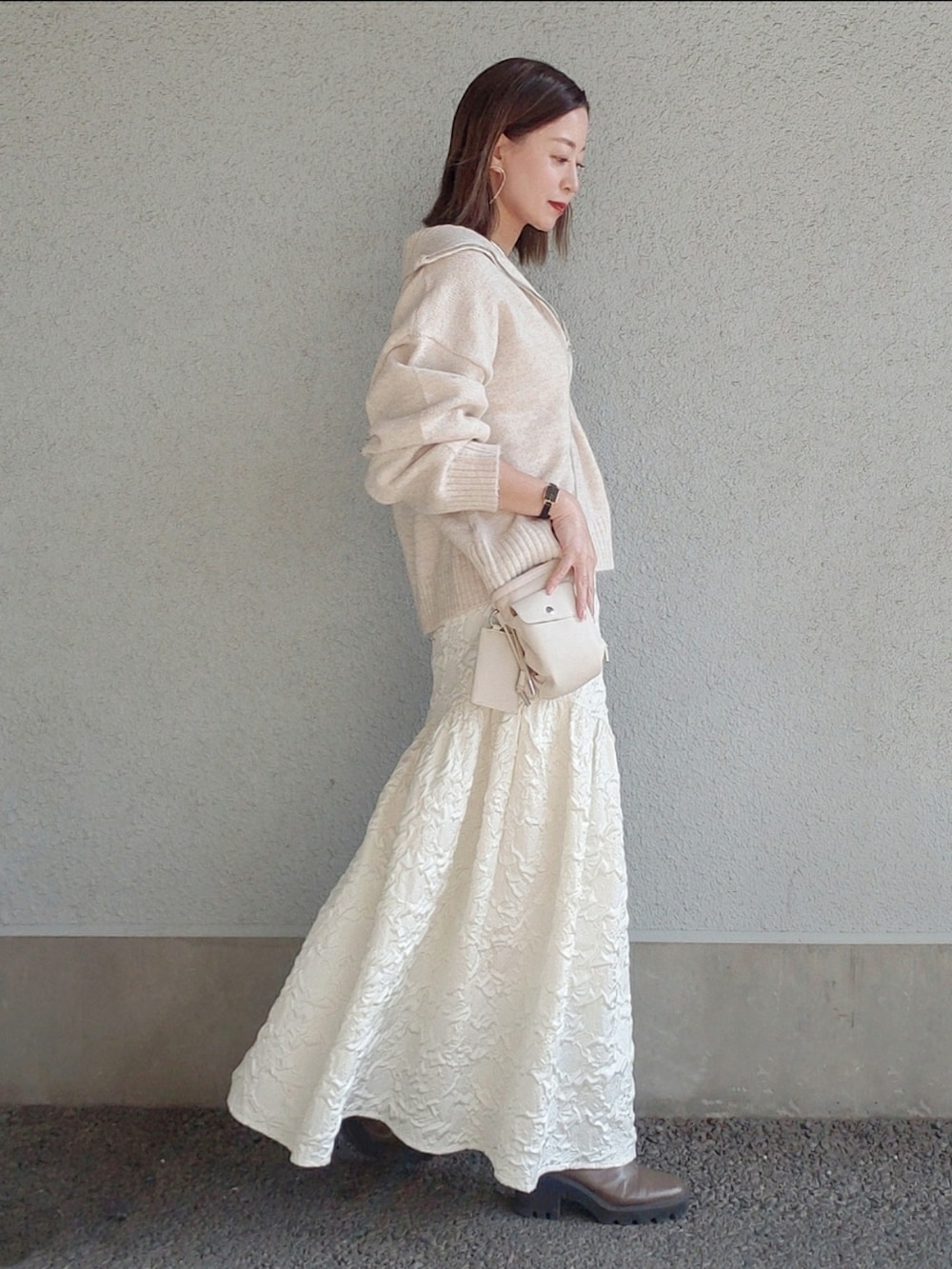 ベージュ系のトップス、ホワイト系のスカート、ベージュ系のブーツを着用したレディースの冬コーディネートの2枚目の写真