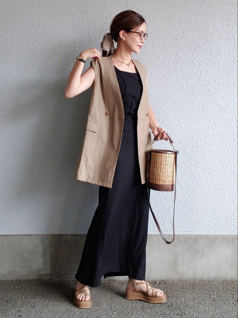 ブラック系のワンピース、ブラウン系のベスト、ブラウン系のサンダルを着用したレディースの夏コーディネートの2枚目の写真