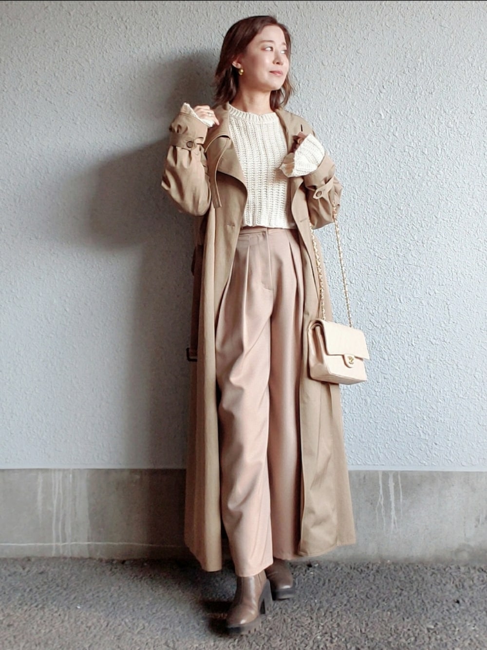 ベージュ系のトレンチコート、ベージュ系のブーツ、ホワイト系のニット/セーターを着用したレディースの冬コーディネートの3枚目の写真