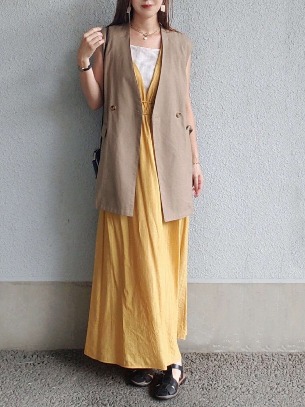 イエロー系のワンピース、ブラウン系のベスト、ブラック系のサンダルを着用したレディースの夏コーディネートの3枚目の写真