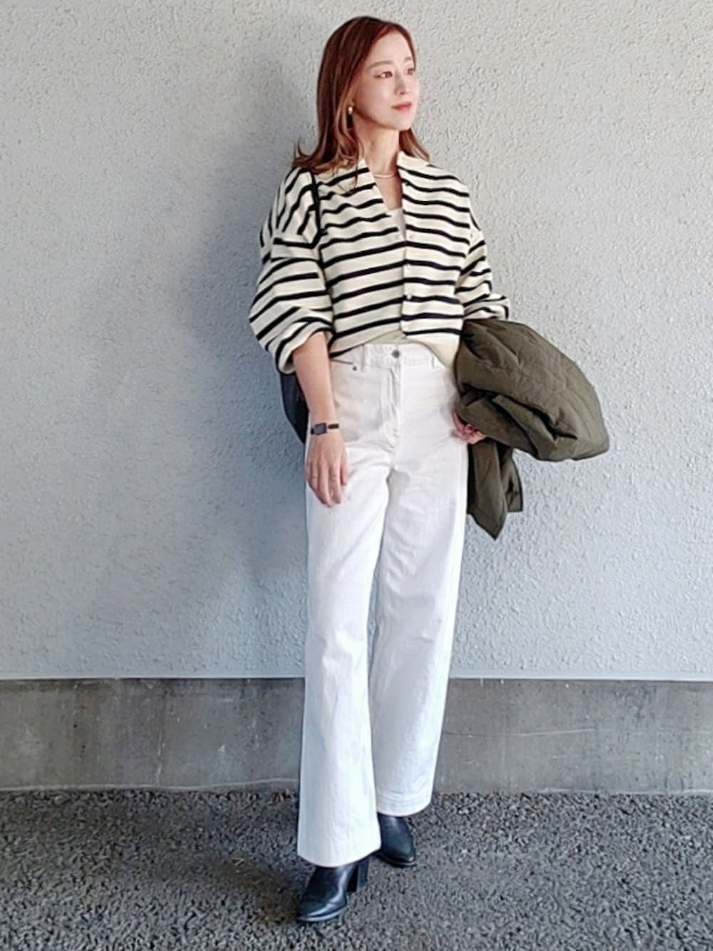 ホワイト系のデニムパンツ、グレー系のカーディガン/ボレロ、グリーン系のダウンベストを着用したレディースの冬コーディネートの2枚目の写真