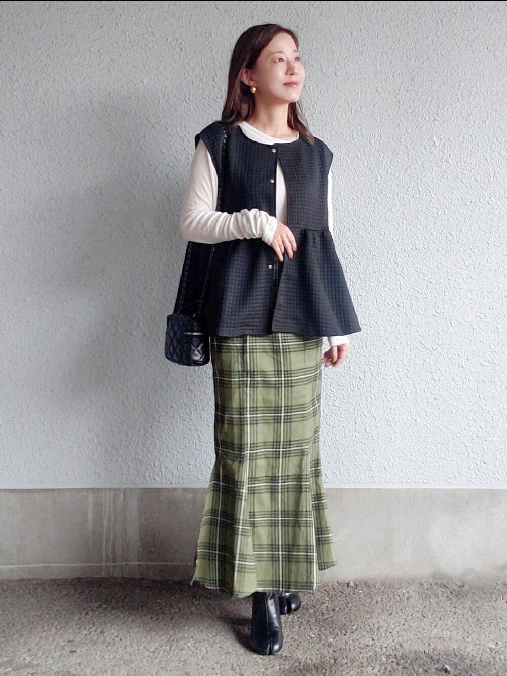 ブラック系のベスト、グリーン系のスカート、ブラック系のブーツを着用したレディースの秋コーディネートの2枚目の写真