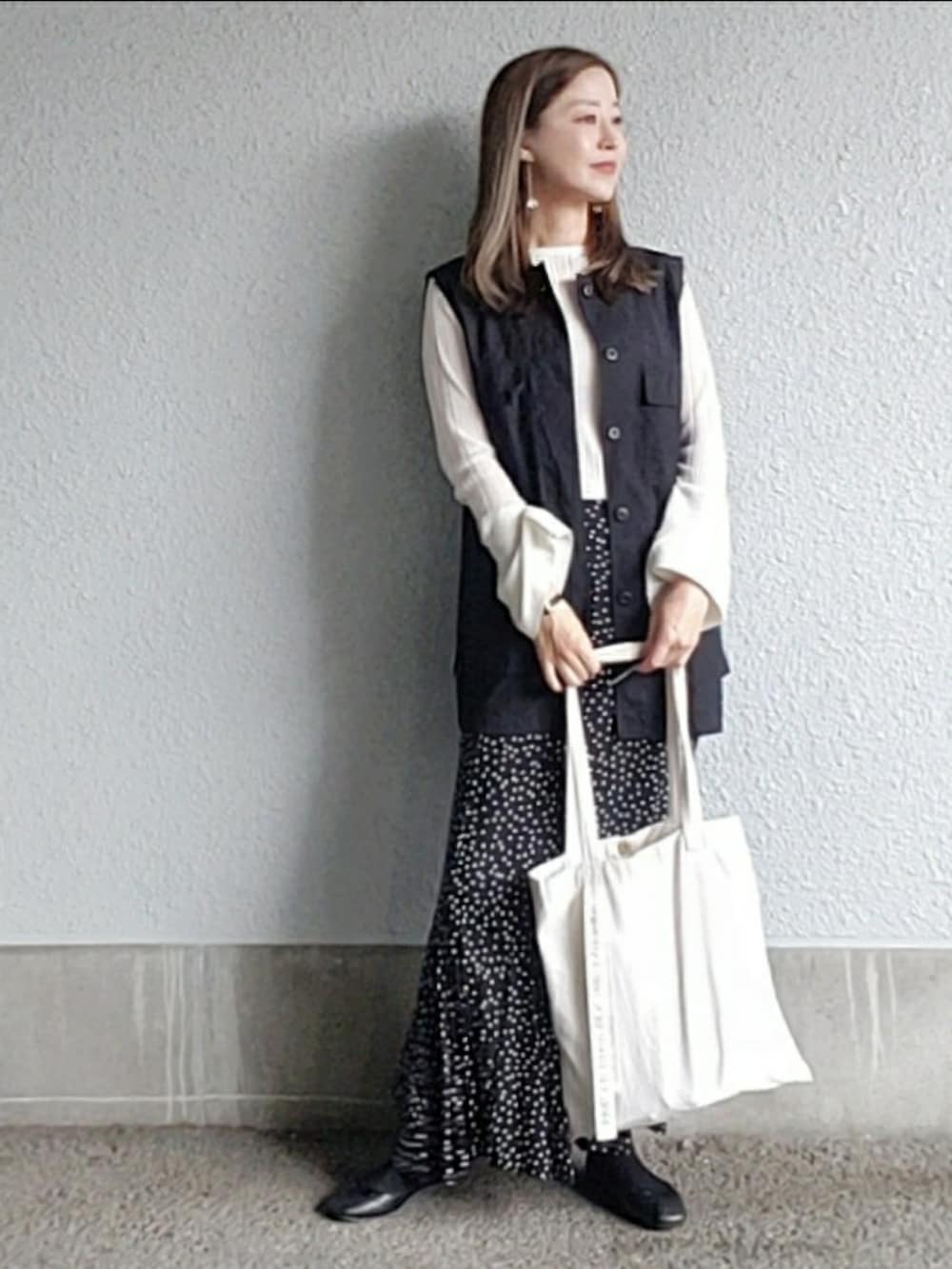 ブラック系のスカート、ブラック系のベスト、ブラック系のバレエシューズを着用したレディースの春コーディネートの2枚目の写真