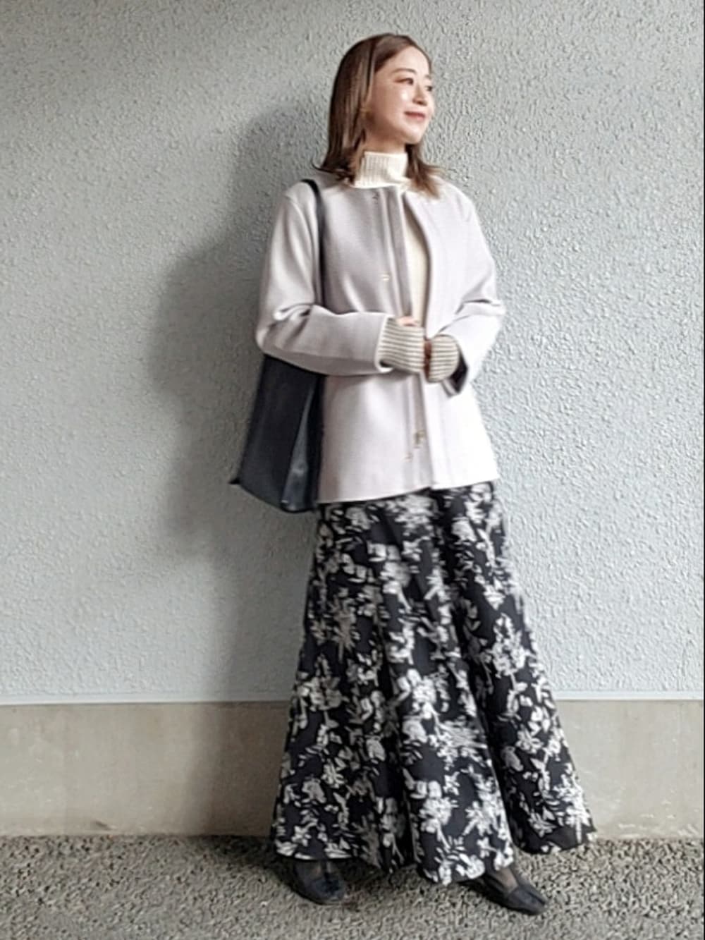 グレー系のノーカラーコート、ブラック系のスカート、ブラック系のブーツを着用したレディースの秋コーディネートの3枚目の写真