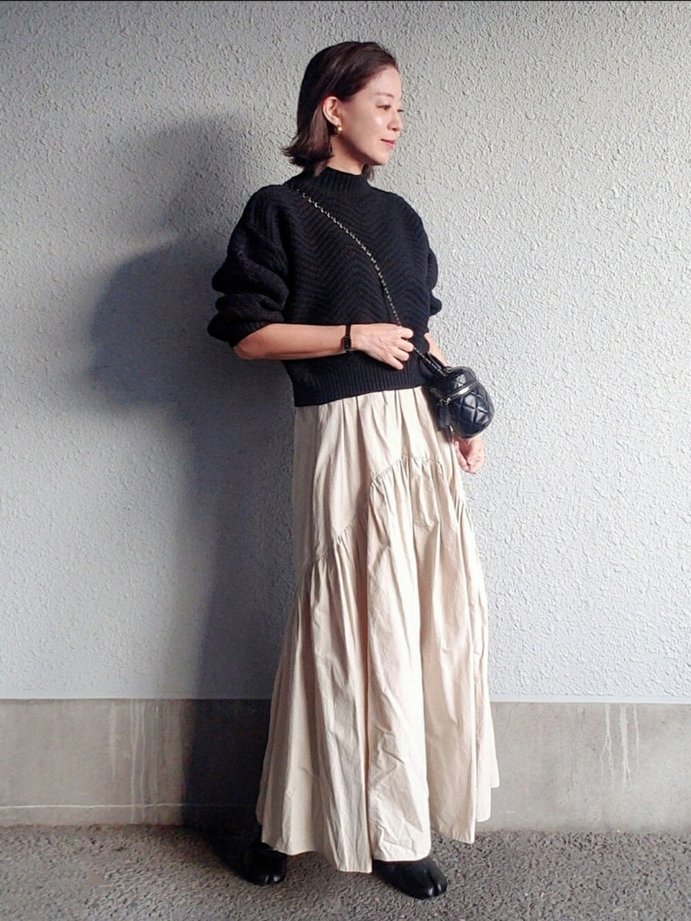 ブラック系のニット/セーター、ブラック系のバッグ、ベージュ系のトレンチコートを着用したレディースの秋コーディネートの3枚目の写真