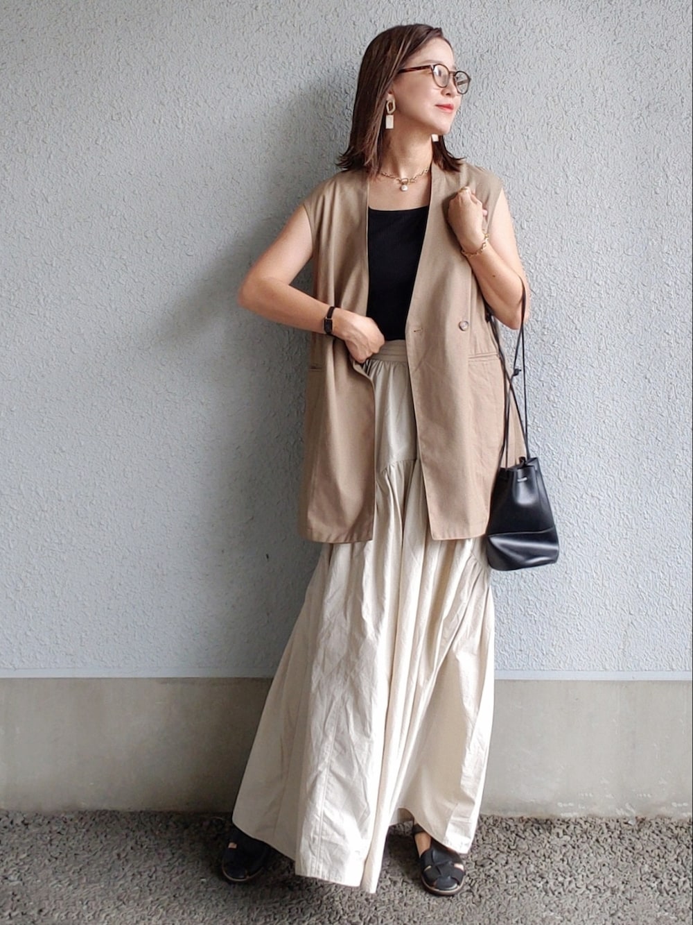 ホワイト系のスカート、ブラック系のタンクトップ、ブラウン系のベストを着用したレディースの夏コーディネートの2枚目の写真