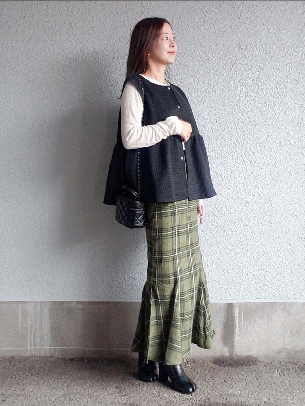 ブラック系のベスト、グリーン系のスカート、ブラック系のブーツを着用したレディースの秋コーディネートの3枚目の写真