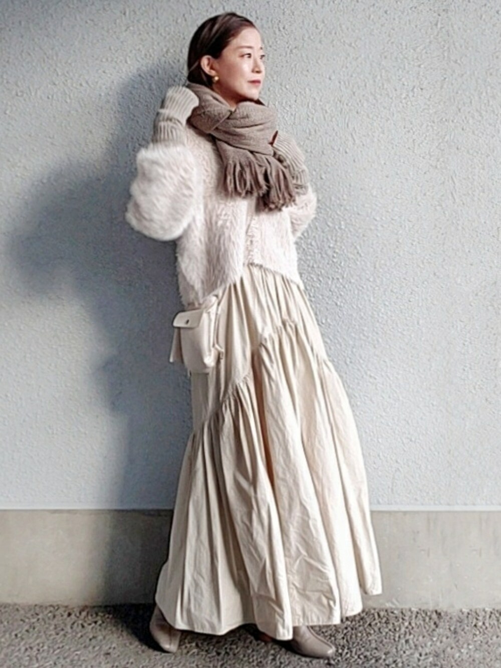 ベージュ系のカーディガン/ボレロ、ホワイト系のスカート、グレー系のブーツを着用したレディースの冬コーディネートの2枚目の写真