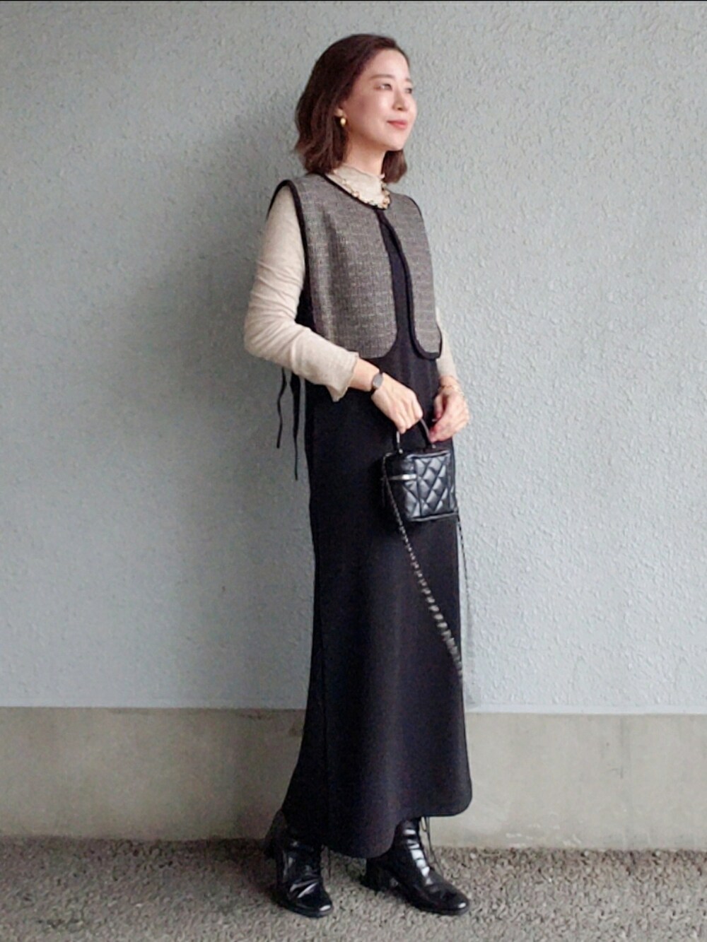 ブラック系のワンピース、ブラック系のベスト、ブラック系のブーツを着用したレディースの冬コーディネートの3枚目の写真