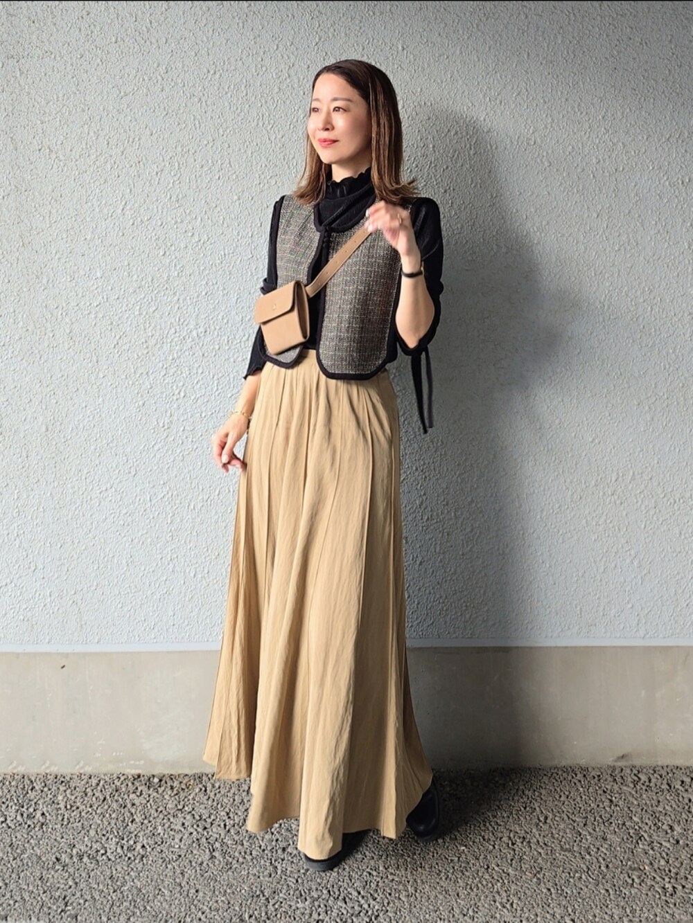 ベージュ系のスカート、ベージュ系のショルダーバッグ、ブラック系のベストを着用したレディースの秋コーディネートの3枚目の写真