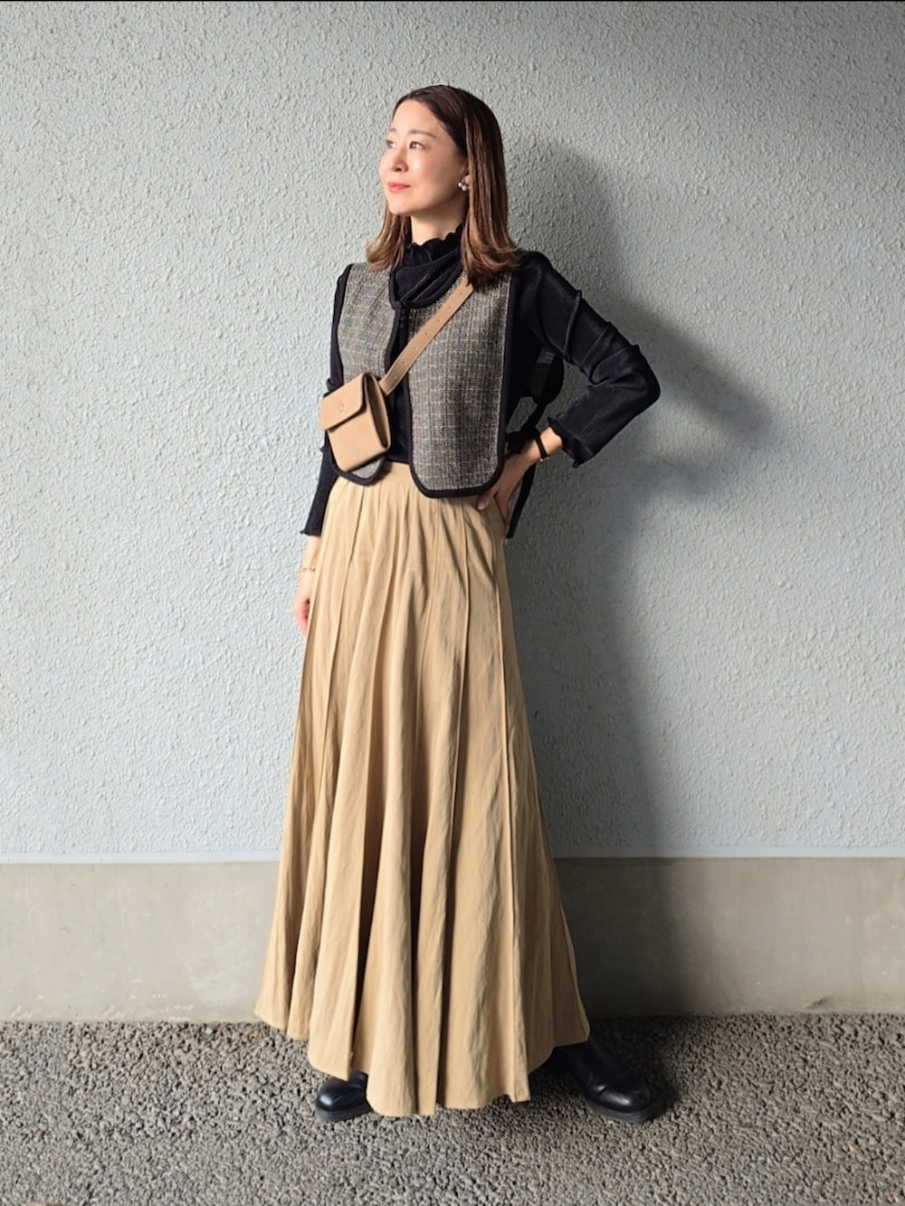 ベージュ系のスカート、ベージュ系のショルダーバッグ、ブラック系のベストを着用したレディースの秋コーディネートの2枚目の写真