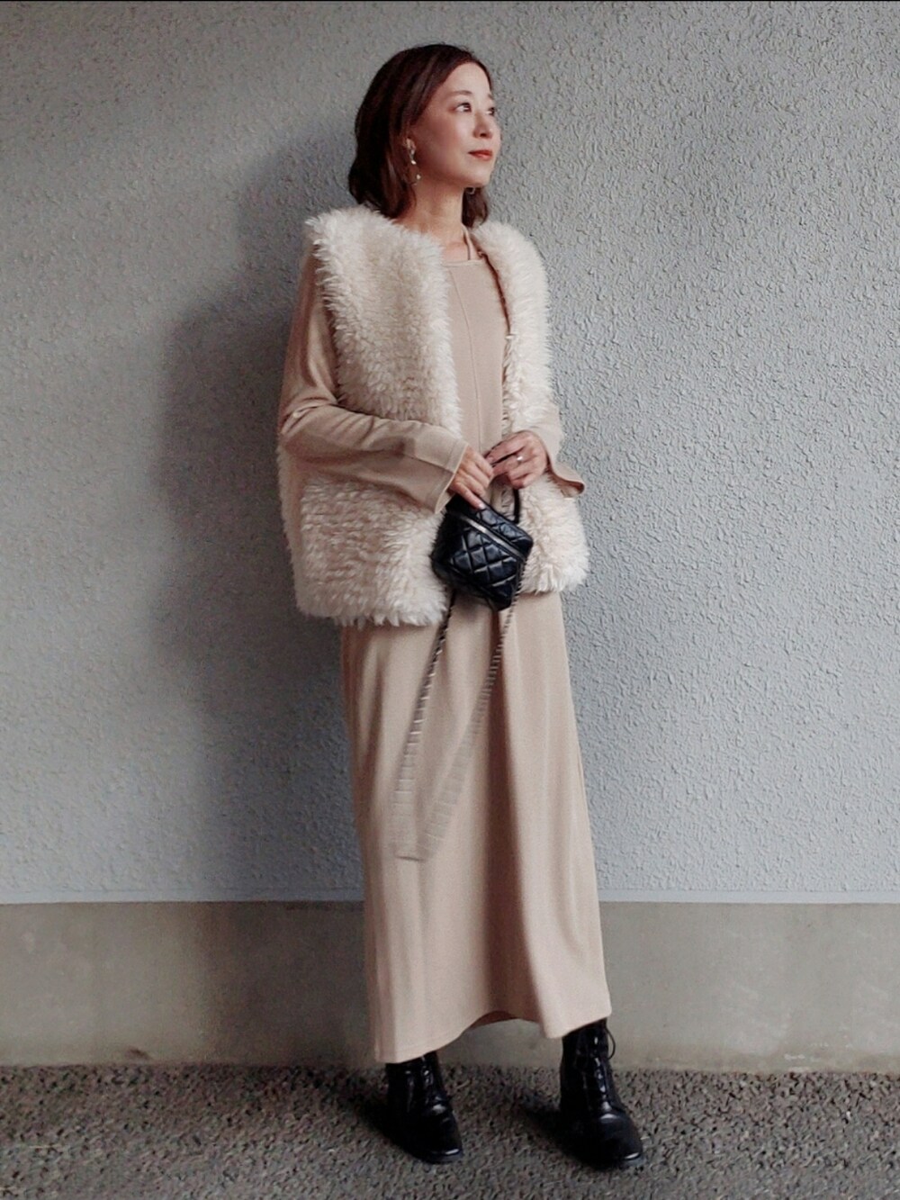 ベージュ系のワンピース、ホワイト系のベスト、ブラック系のブーツを着用したレディースの冬コーディネートの3枚目の写真