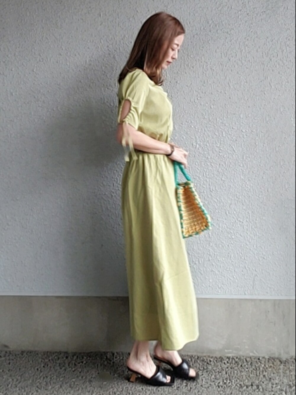 グリーン系のワンピース、イエロー系のバッグ、ブラック系のサンダルを着用したレディースの春コーディネートの3枚目の写真