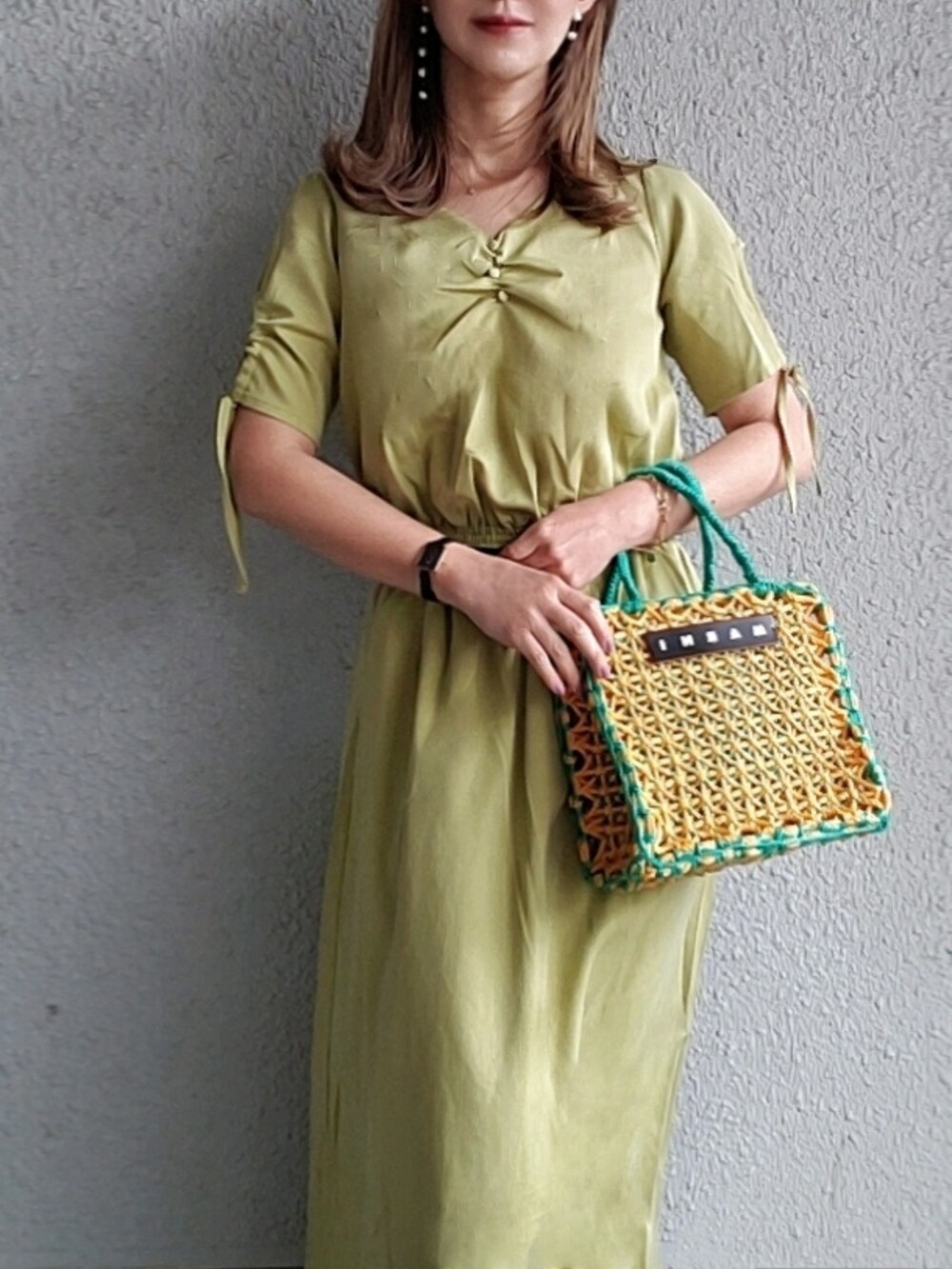 グリーン系のワンピース、イエロー系のバッグ、ブラック系のサンダルを着用したレディースの春コーディネートの2枚目の写真