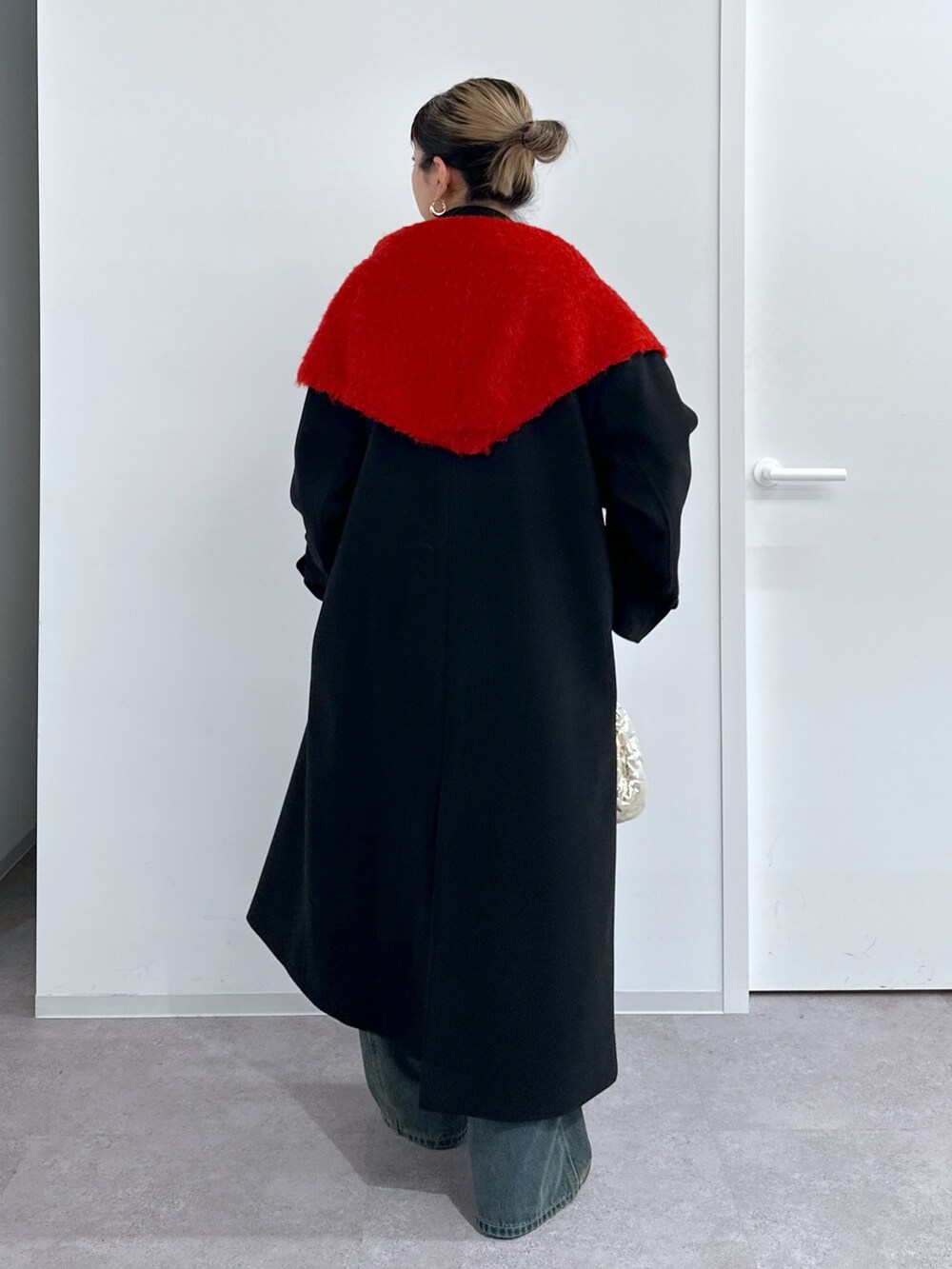 ブラック系のチェスターコート、レッド系のニット/セーター、ブルー系のデニムパンツを着用したレディースの冬コーディネートの3枚目の写真