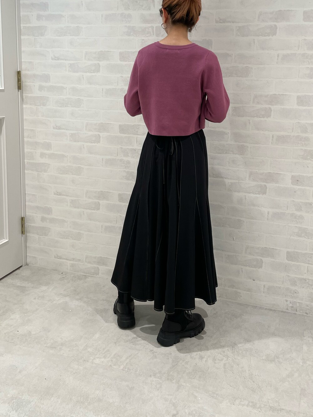 ブラック系のスカート、パープル系のニット/セーター、ブラック系のブーツを着用したレディースの秋コーディネートの3枚目の写真