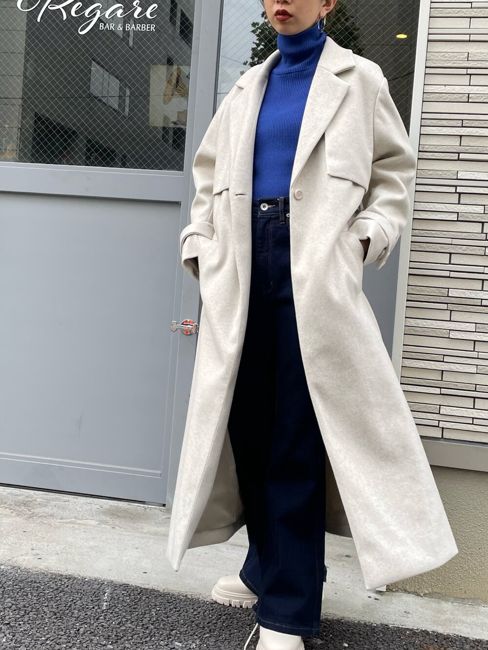 ベージュ系のチェスターコート、ブルー系のニット/セーター、ブルー系のデニムパンツを着用したレディースの秋コーディネートの3枚目の写真