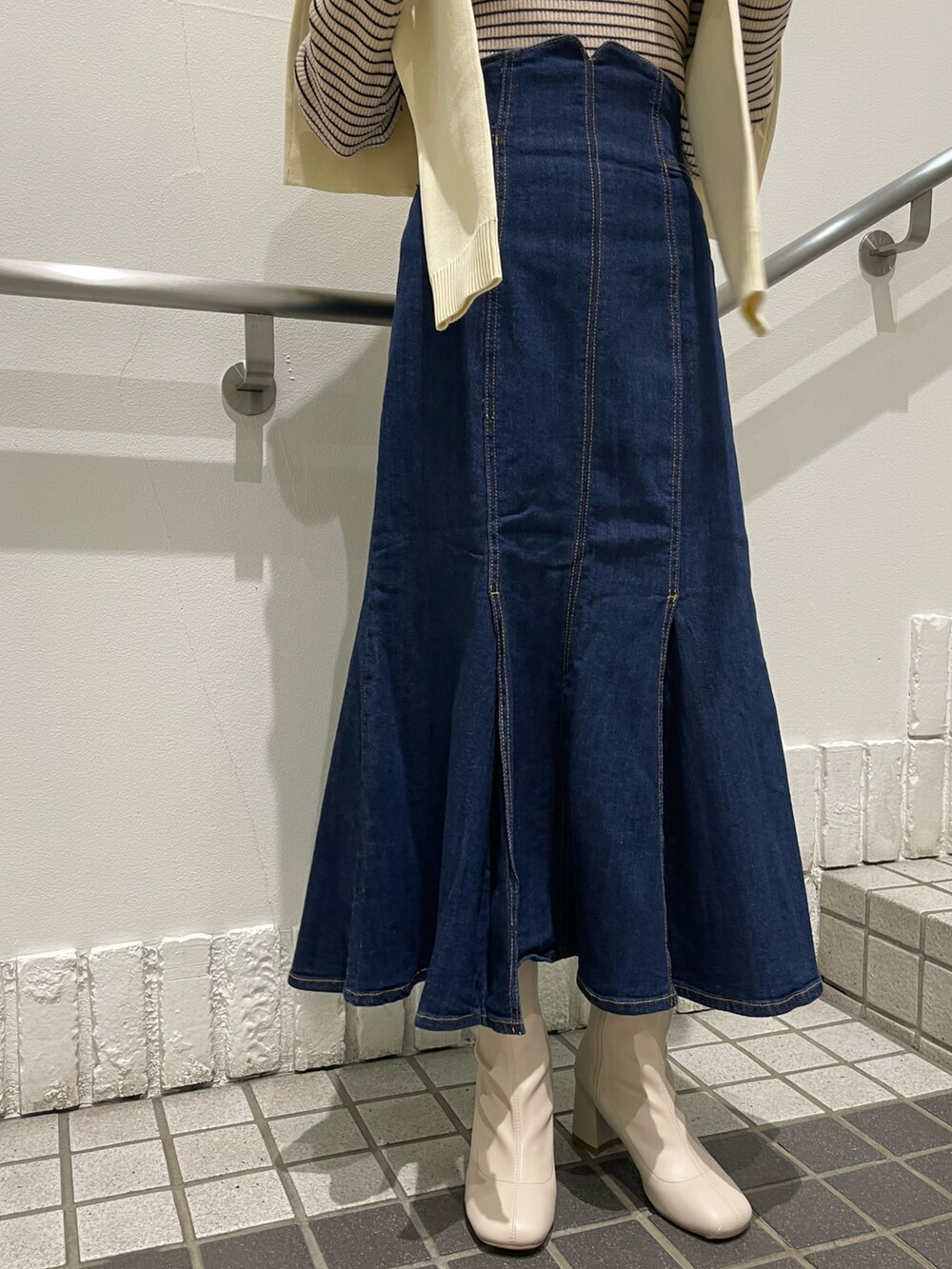 ブルー系のデニムスカート、ホワイト系のニット/セーター、ホワイト系のブーツを着用したレディースの秋コーディネートの4枚目の写真