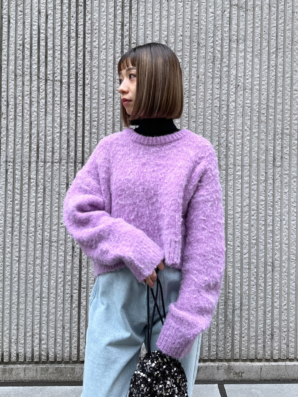パープル系のニット/セーター、ブルー系のデニムパンツ、ブラック系のハンドバッグを着用したレディースの冬コーディネートの5枚目の写真