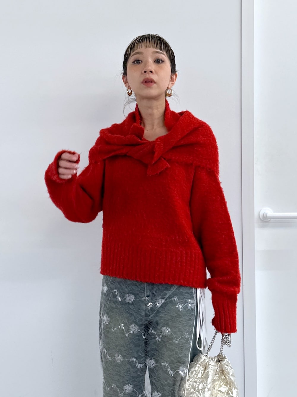 ブラック系のチェスターコート、レッド系のニット/セーター、ブルー系のデニムパンツを着用したレディースの冬コーディネートの6枚目の写真