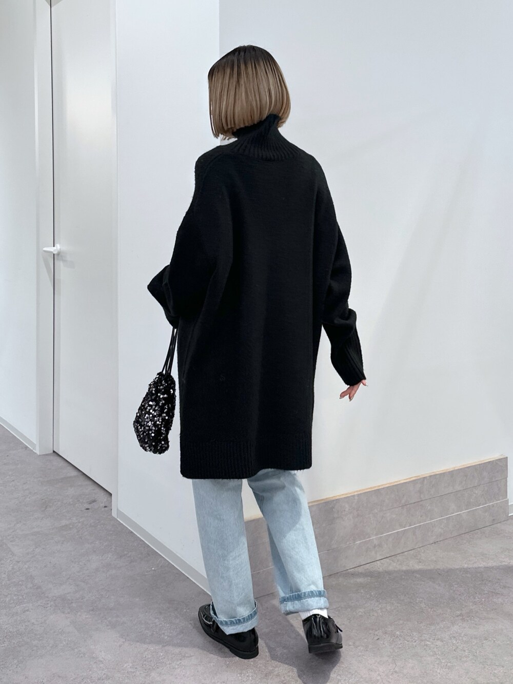 ブラック系のニット/セーター、ブラック系のハンドバッグ、ブルー系のデニムパンツを着用したレディースの冬コーディネートの3枚目の写真