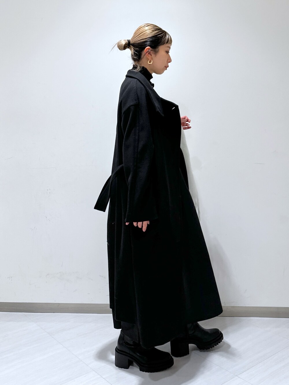 ブラック系のステンカラーコート、ブラック系のワンピース、ブラック系のTシャツ/カットソーを着用したレディースの冬コーディネートの2枚目の写真