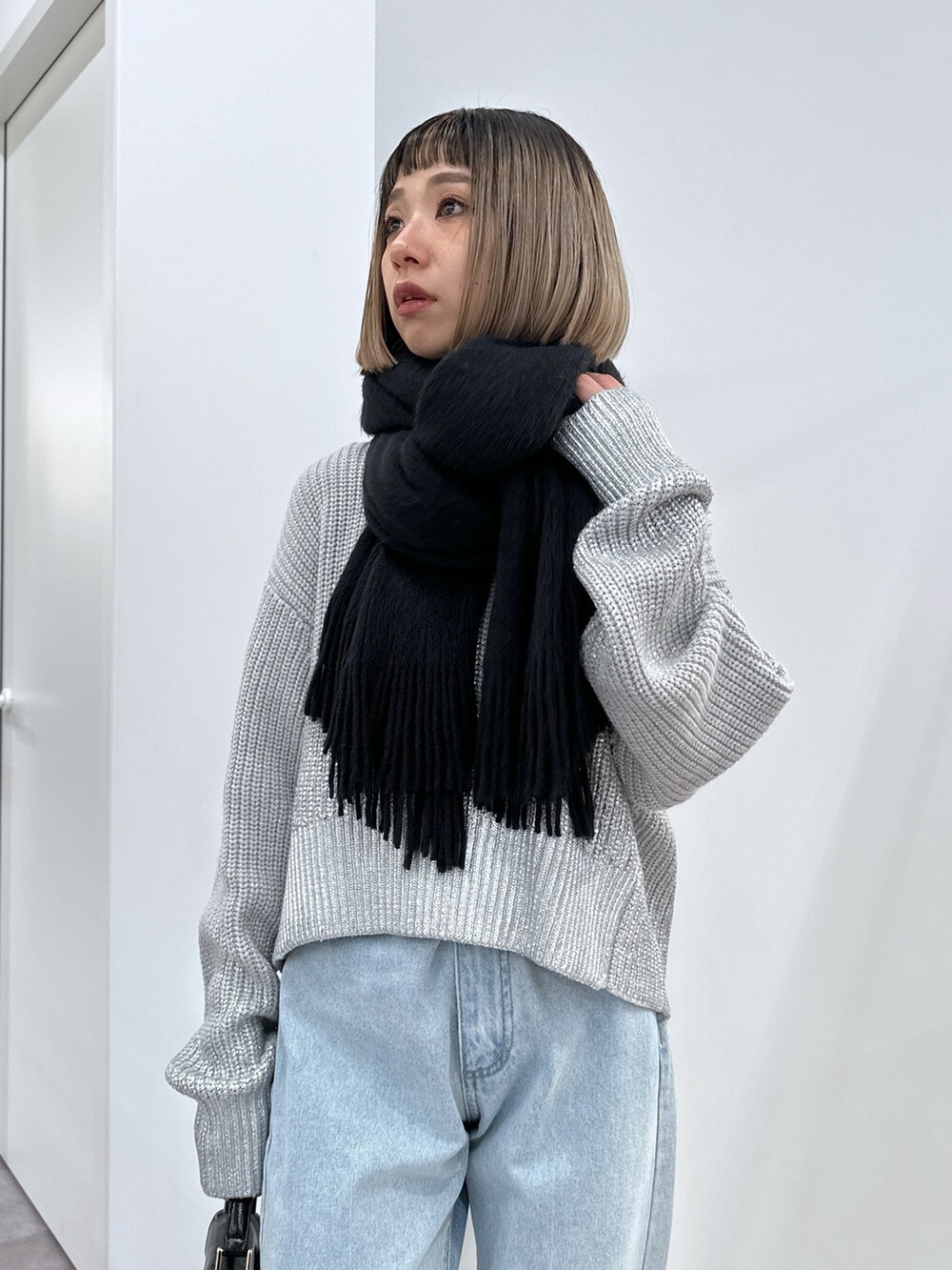 グレー系のニット/セーター、ブルー系のデニムパンツ、ブラック系のショルダーバッグを着用したレディースの冬コーディネートの4枚目の写真