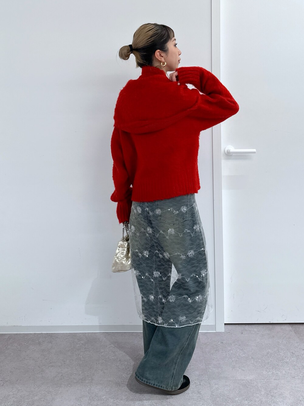 ブラック系のチェスターコート、レッド系のニット/セーター、ブルー系のデニムパンツを着用したレディースの冬コーディネートの5枚目の写真