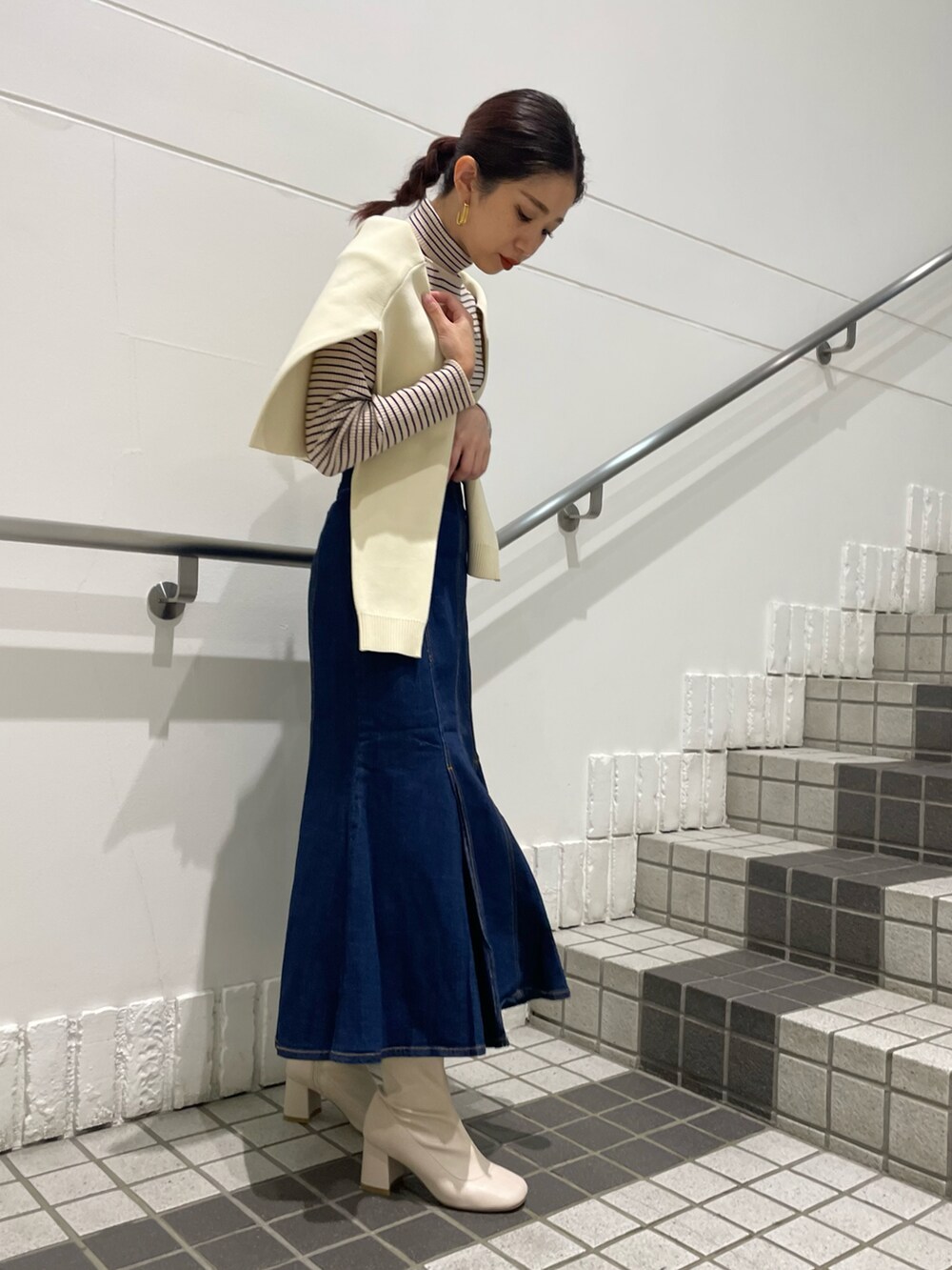 ブルー系のデニムスカート、ホワイト系のニット/セーター、ホワイト系のブーツを着用したレディースの秋コーディネートの2枚目の写真