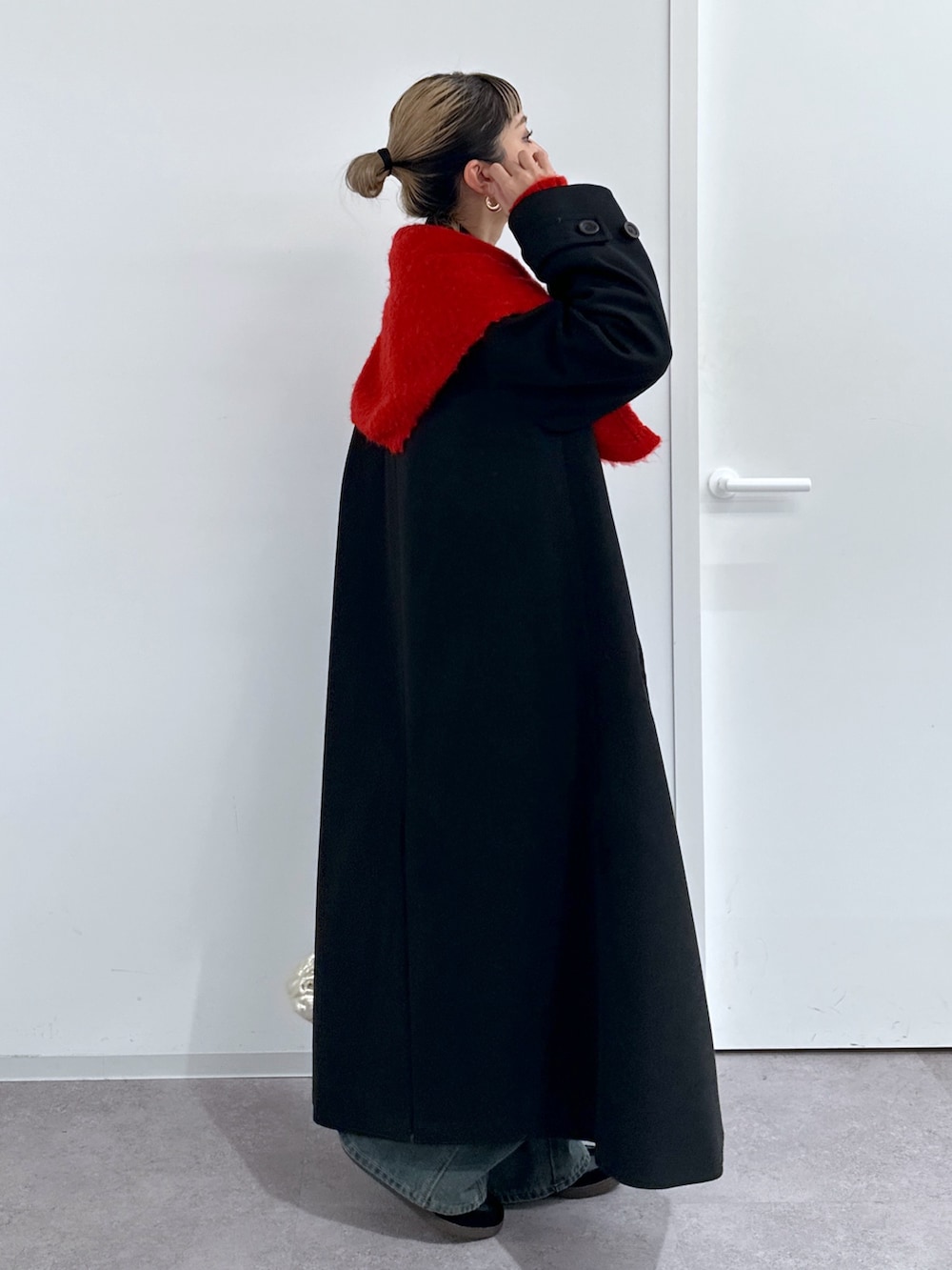 ブラック系のチェスターコート、レッド系のニット/セーター、ブルー系のデニムパンツを着用したレディースの冬コーディネートの2枚目の写真