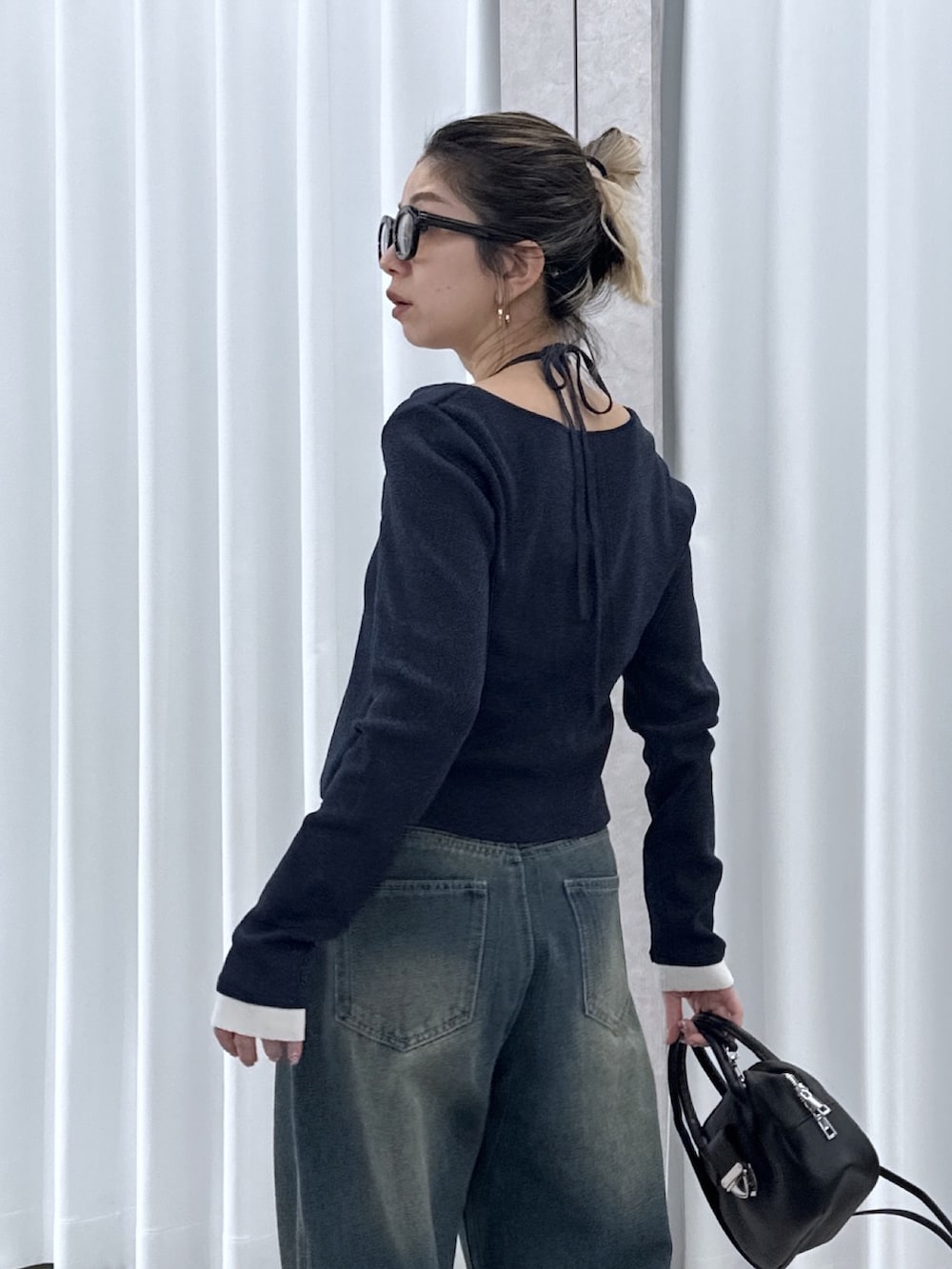 ブルー系のニット/セーター、ブルー系のデニムパンツ、ブラック系のハンドバッグを着用したレディースの春コーディネートの5枚目の写真