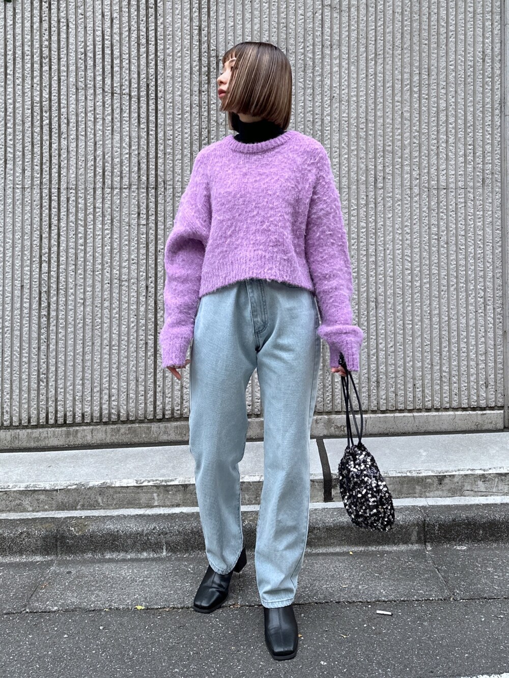 パープル系のニット/セーター、ブルー系のデニムパンツ、ブラック系のハンドバッグを着用したレディースの冬コーディネートの2枚目の写真
