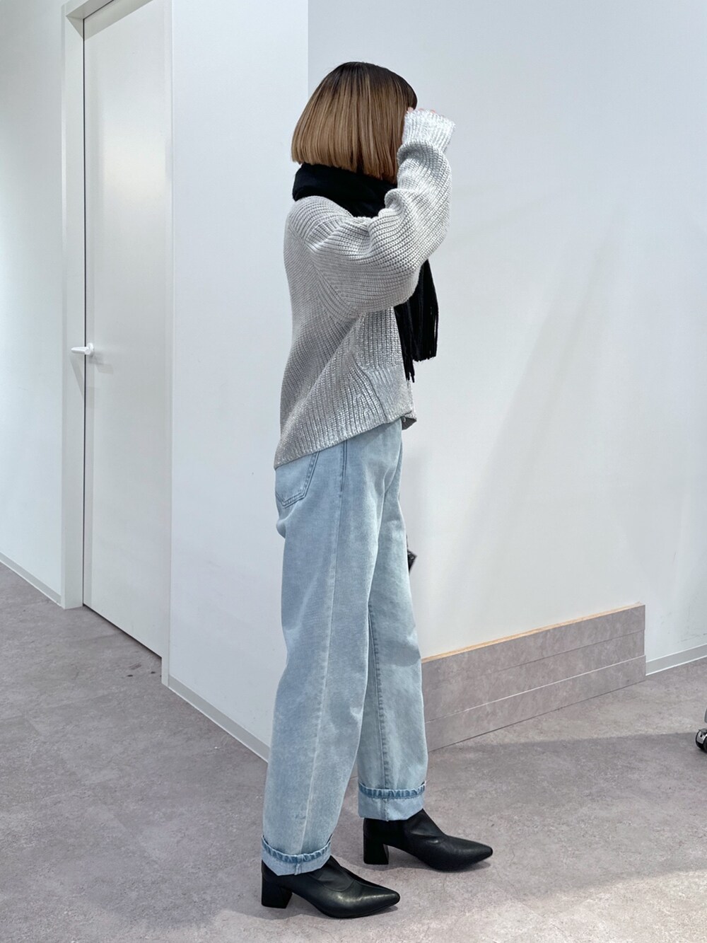 グレー系のニット/セーター、ブルー系のデニムパンツ、ブラック系のショルダーバッグを着用したレディースの冬コーディネートの2枚目の写真