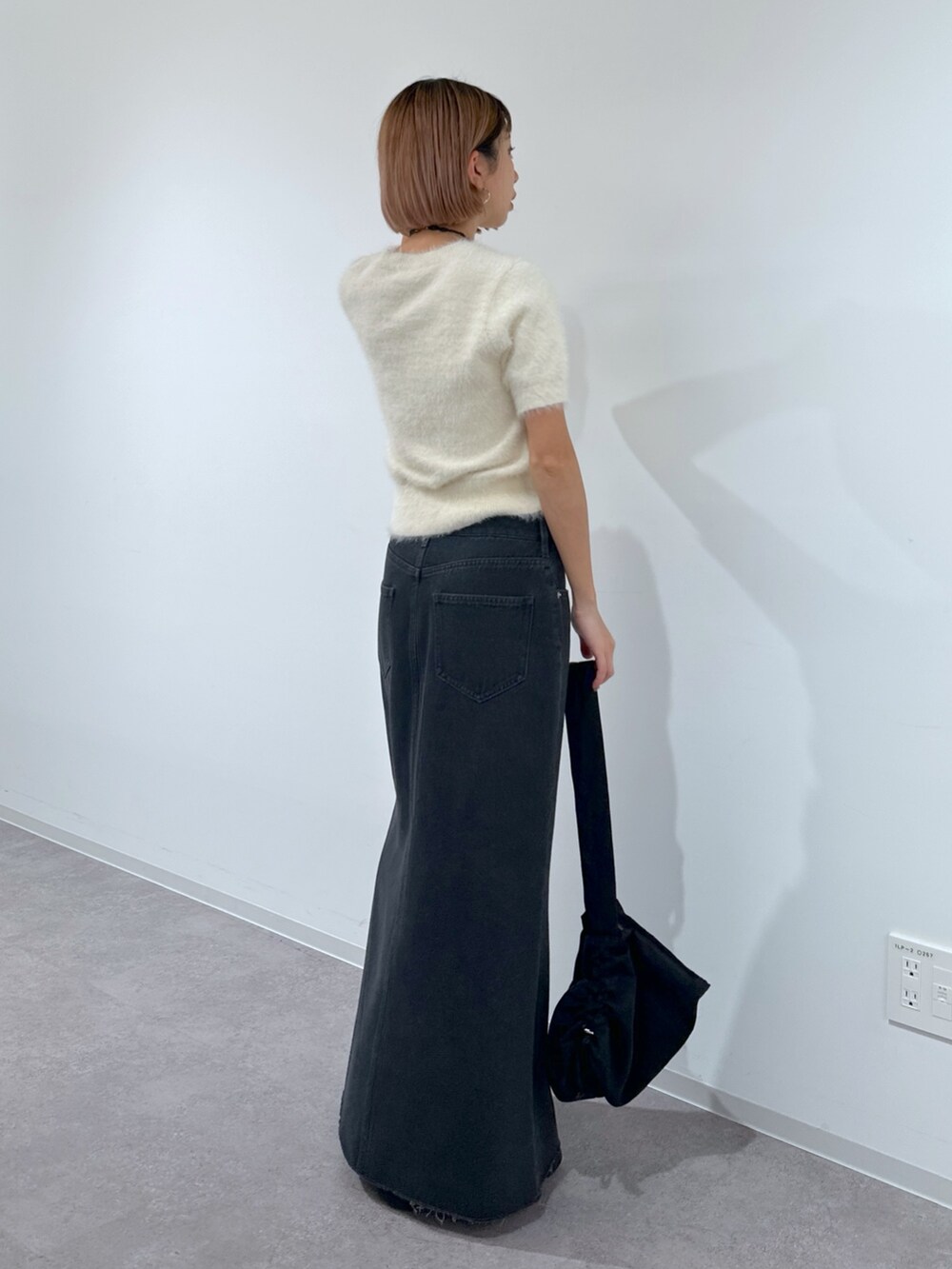 ブラック系のショルダーバッグ、ホワイト系のニット/セーター、ブラック系のデニムスカートを着用したレディースの春コーディネートの3枚目の写真